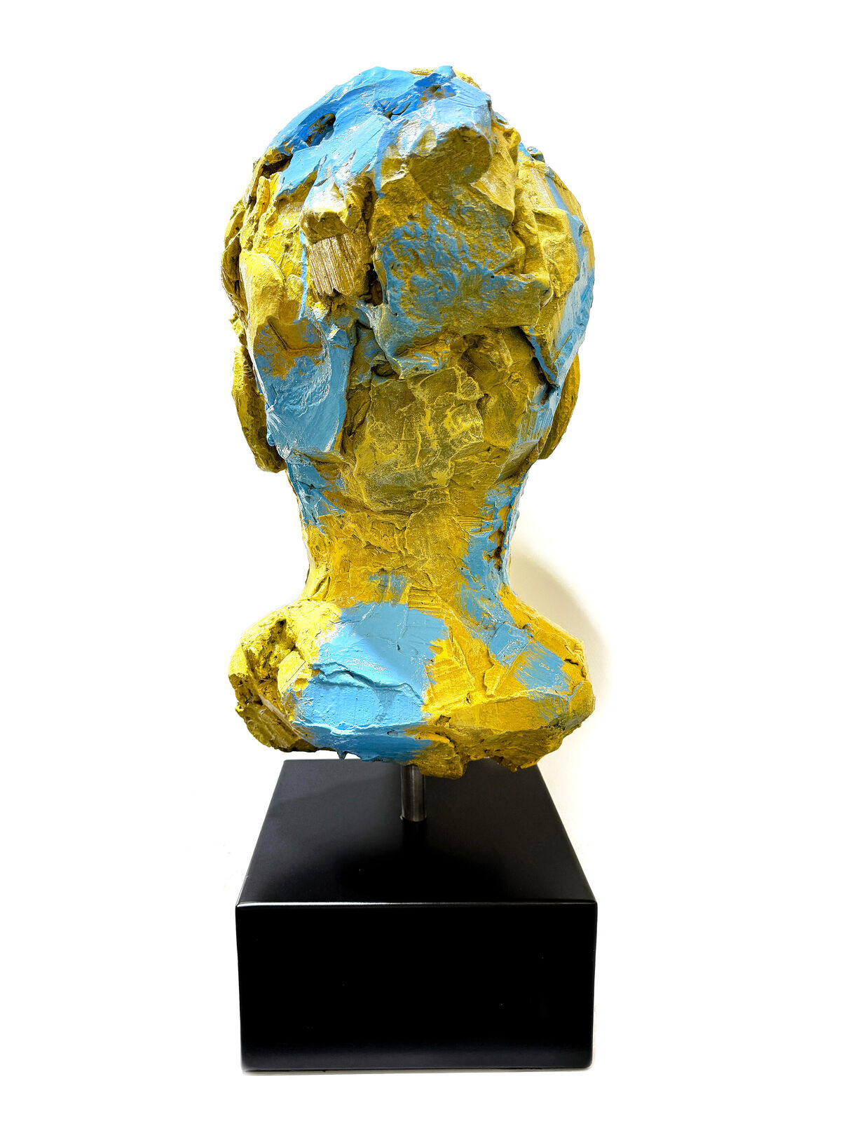 A yellow and blue sculpture of a woman's face on a black stand.