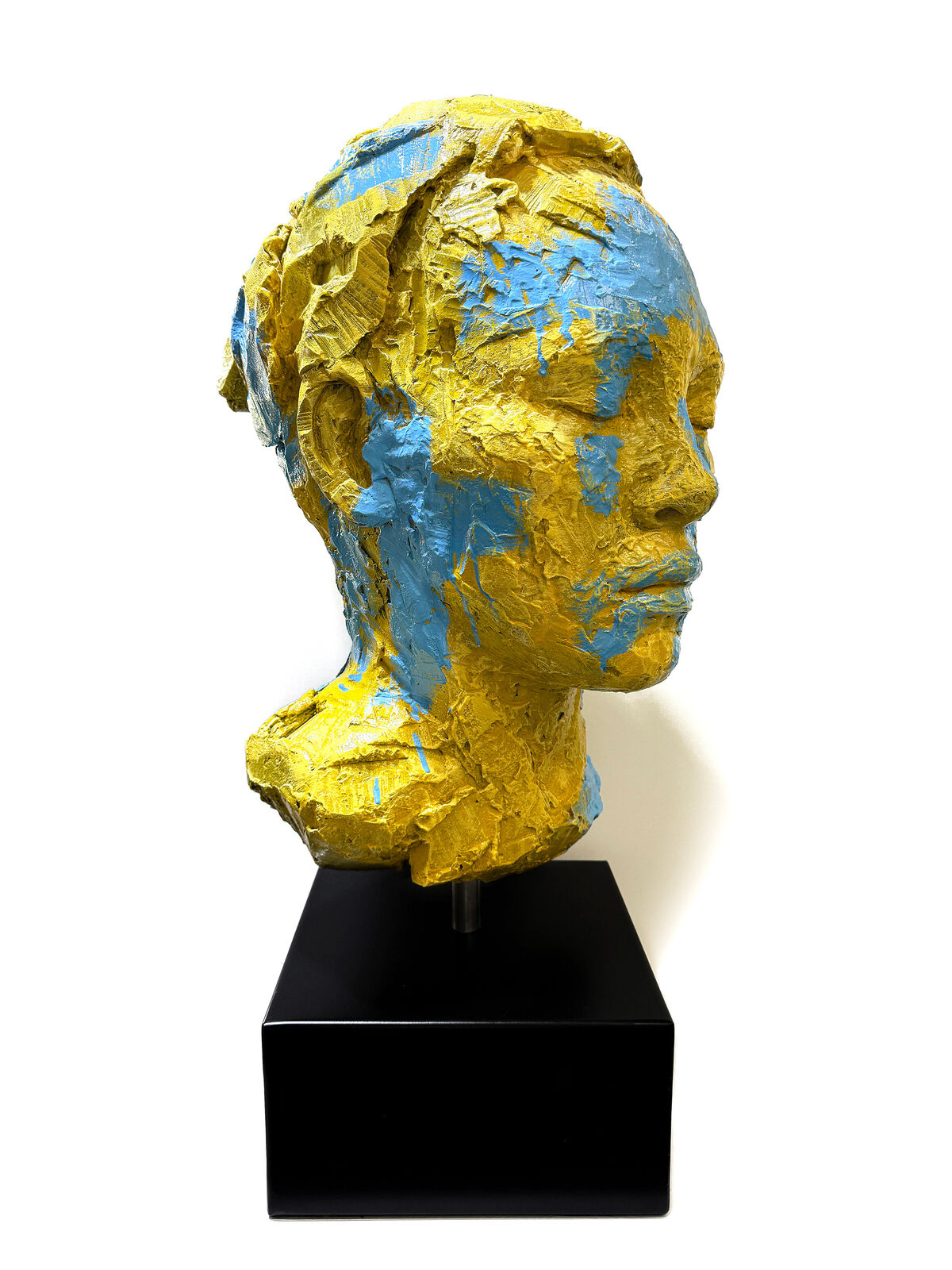 A yellow and blue sculpture of a woman's face on a black stand.