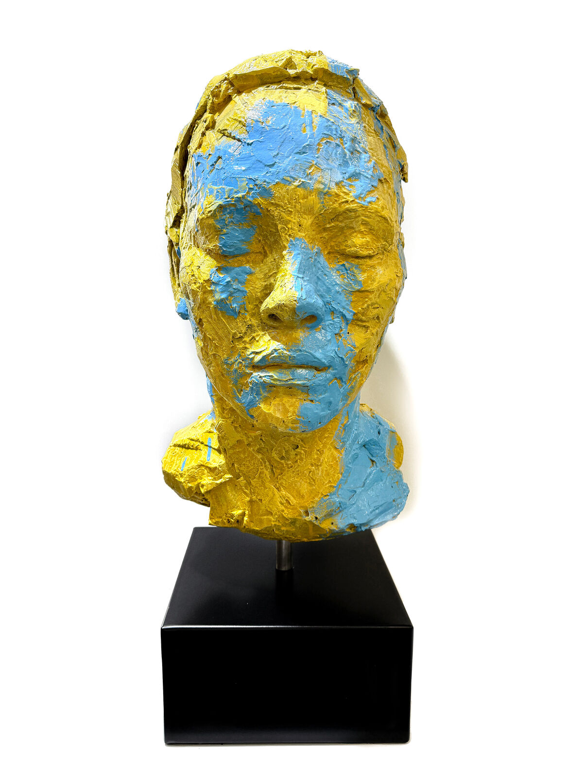 A yellow and blue sculpture of a woman's face on a black stand.