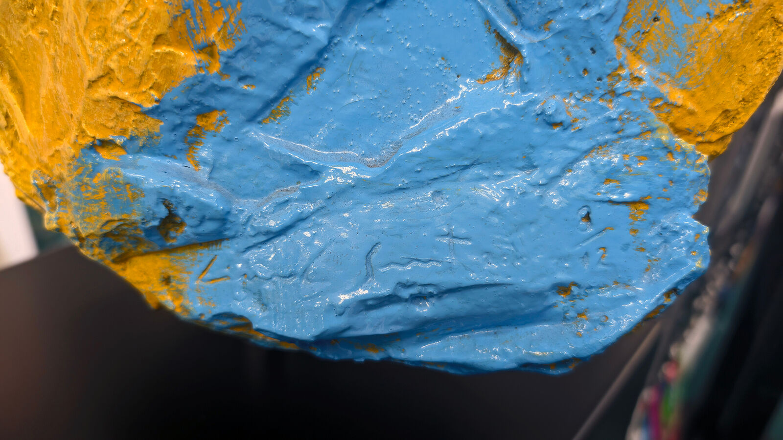 A yellow and blue sculpture of a woman's face on a black stand.