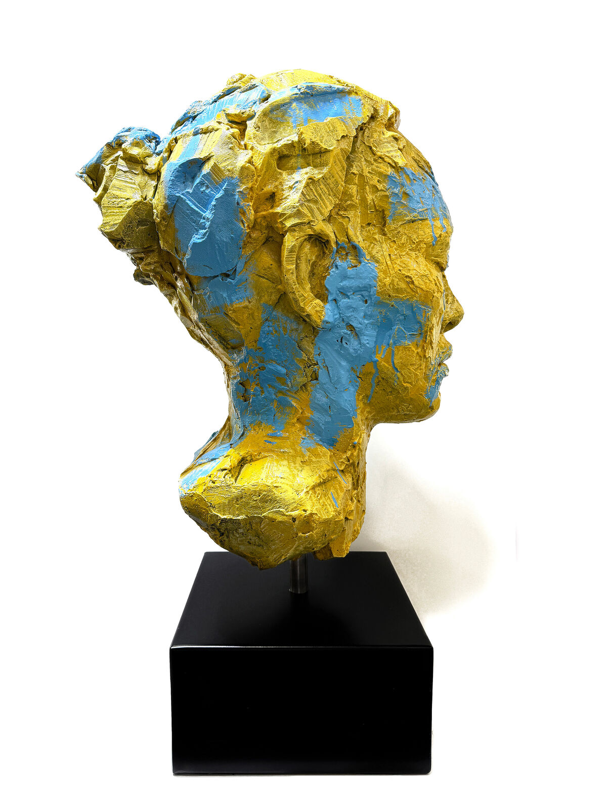 A yellow and blue sculpture of a woman's face on a black stand.