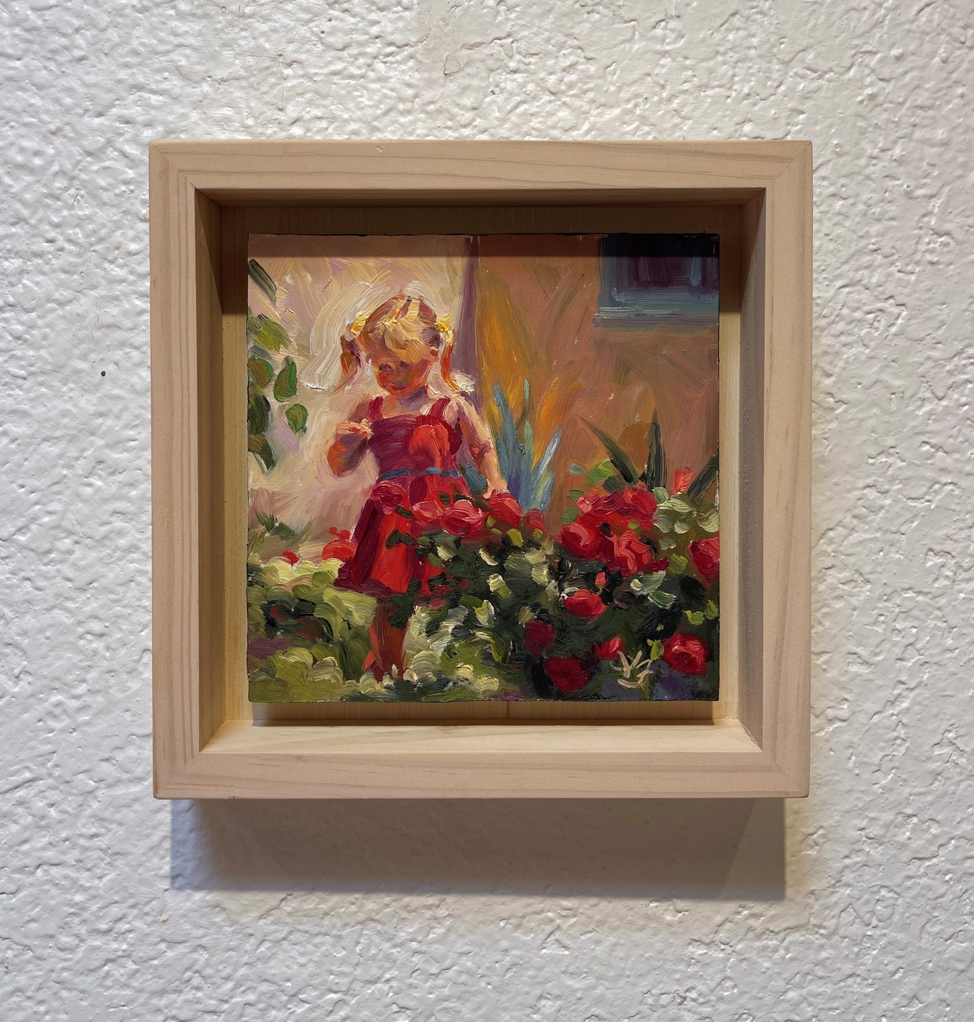 A child in a red dress stands amidst blooming roses in a sunlit garden.