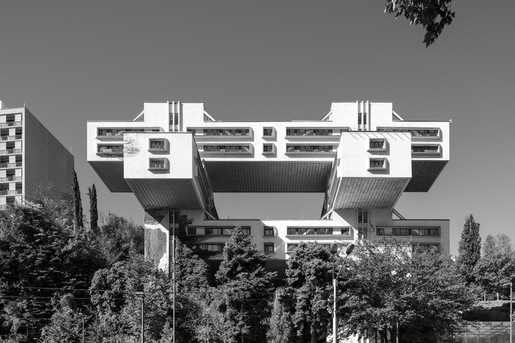 A black-and-white architectural photograph of a massive, floating building suspended over a hillside.