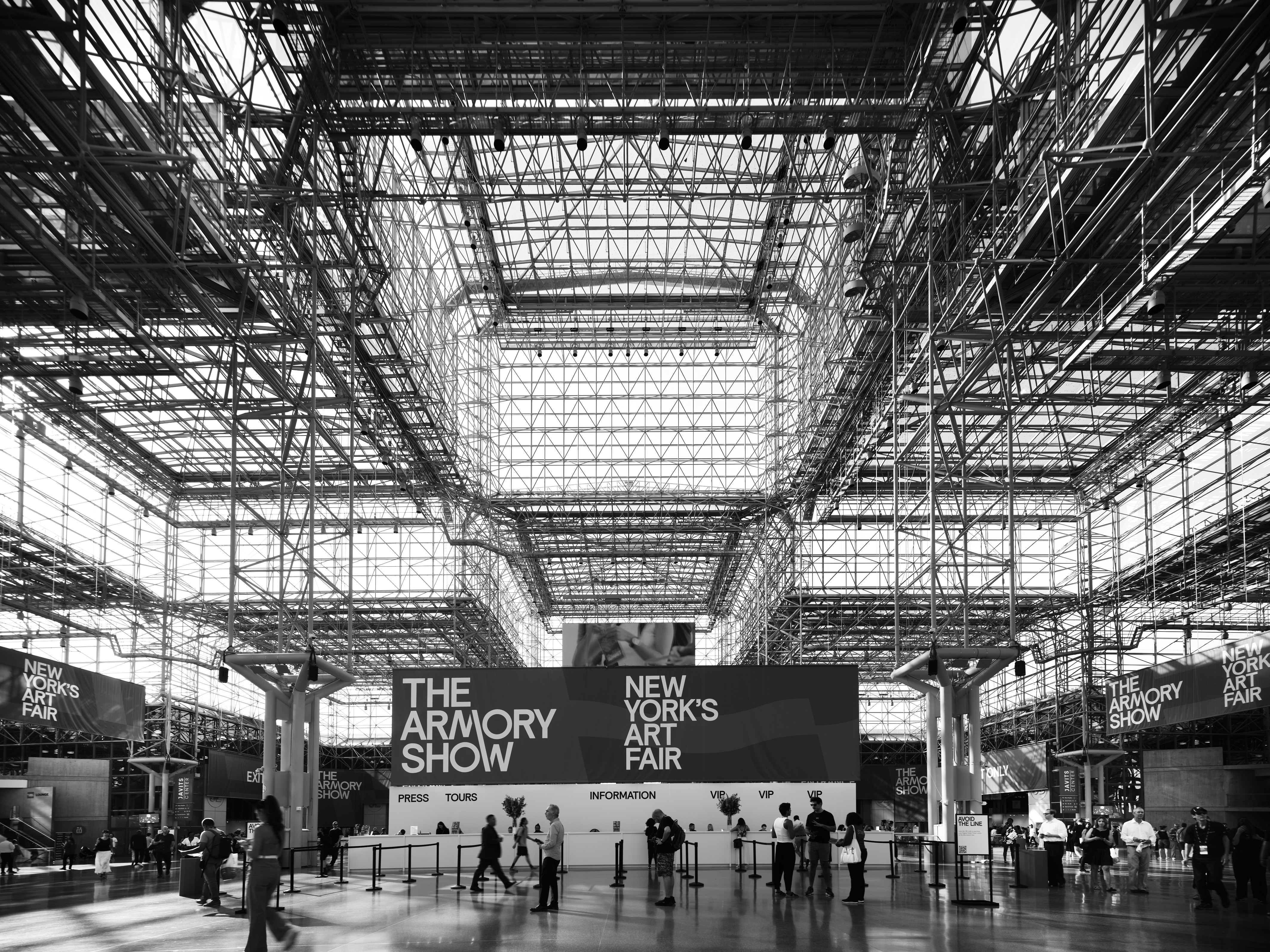 A black and white photo of people walking through a large building.