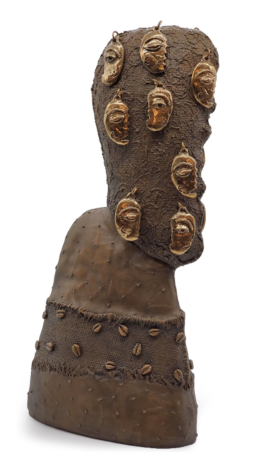 A textured bronze bust adorned with multiple gold masks and scattered cowrie shells.