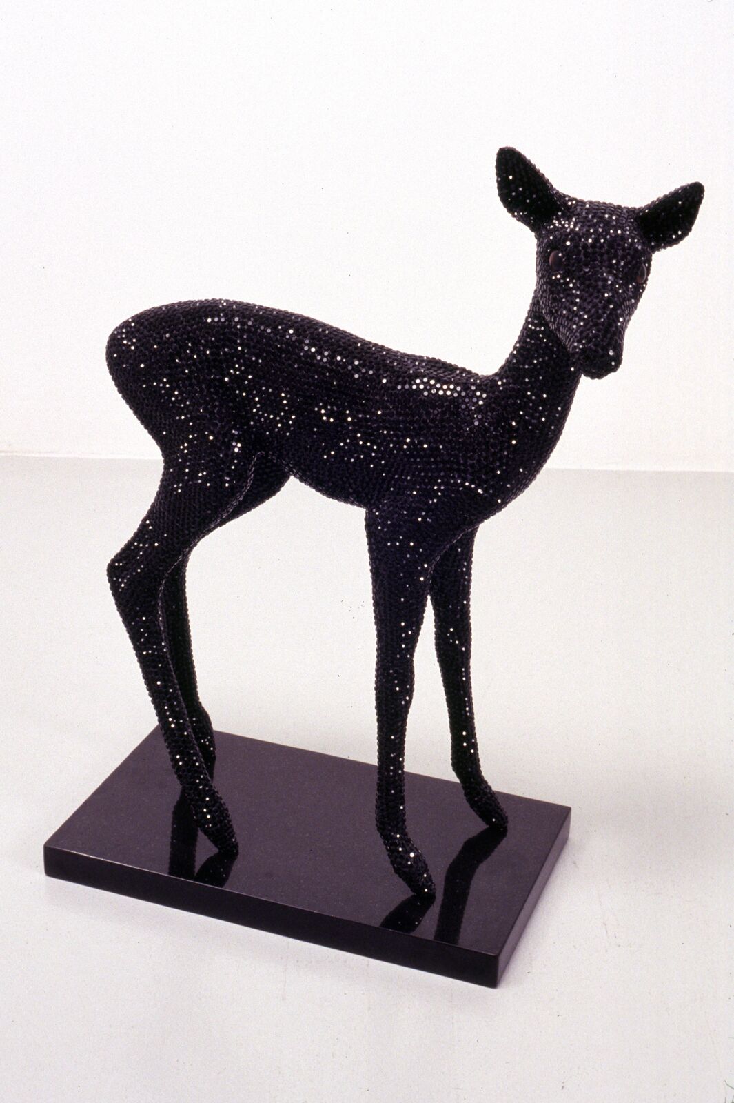 A black fawn sculpture covered in sparkling sequins standing on a glossy black base.