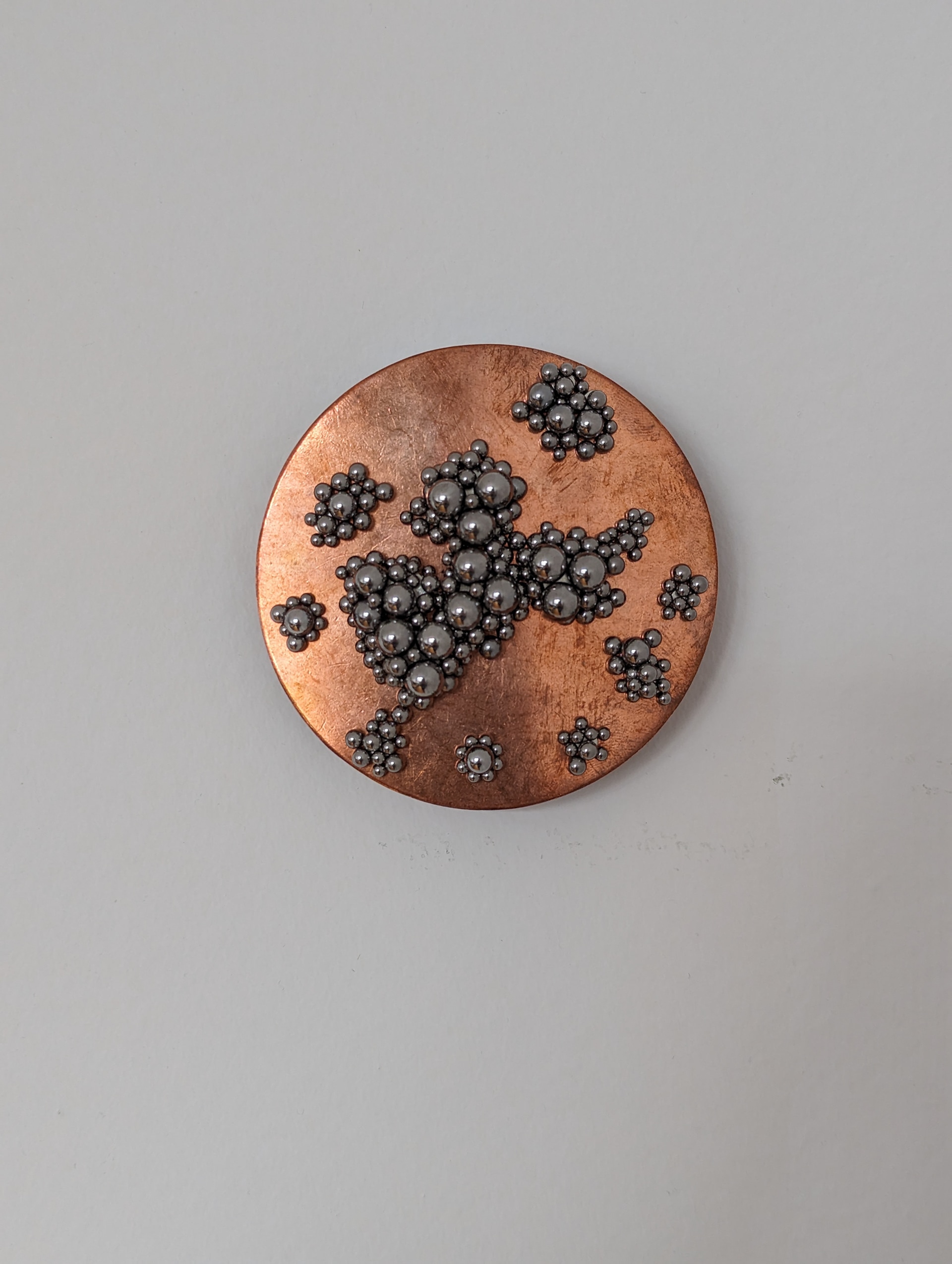 A copper and silver brooch on a white surface.