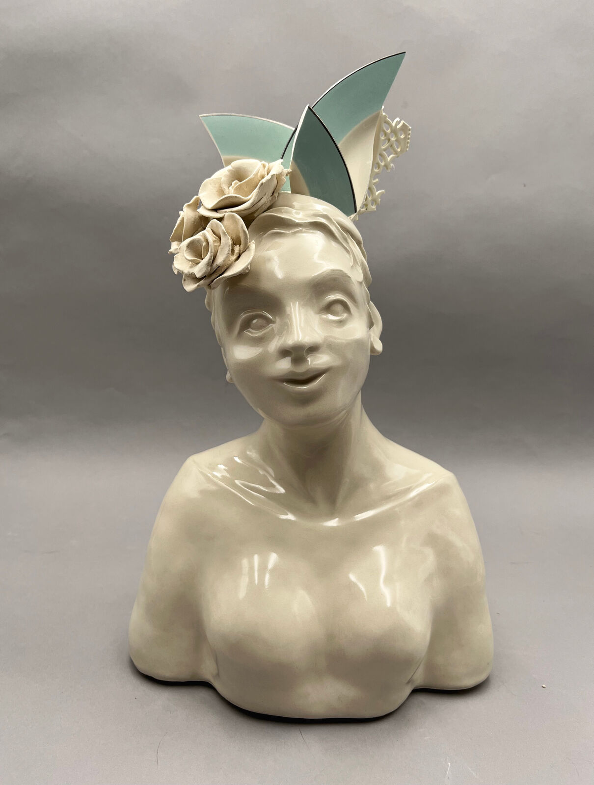 A glossy ceramic bust of a smiling figure adorned with sculpted flowers and geometric cat-ear shapes.
