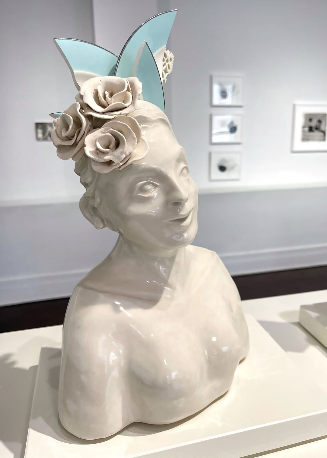 A glossy ceramic bust of a smiling figure adorned with sculpted flowers and geometric cat-ear shapes.
