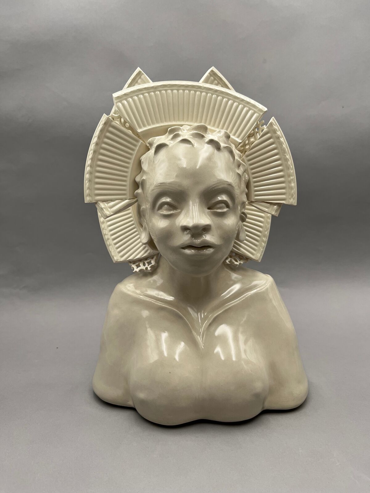 A glossy ceramic bust of a figure with an elaborate, segmented crown-like headpiece.