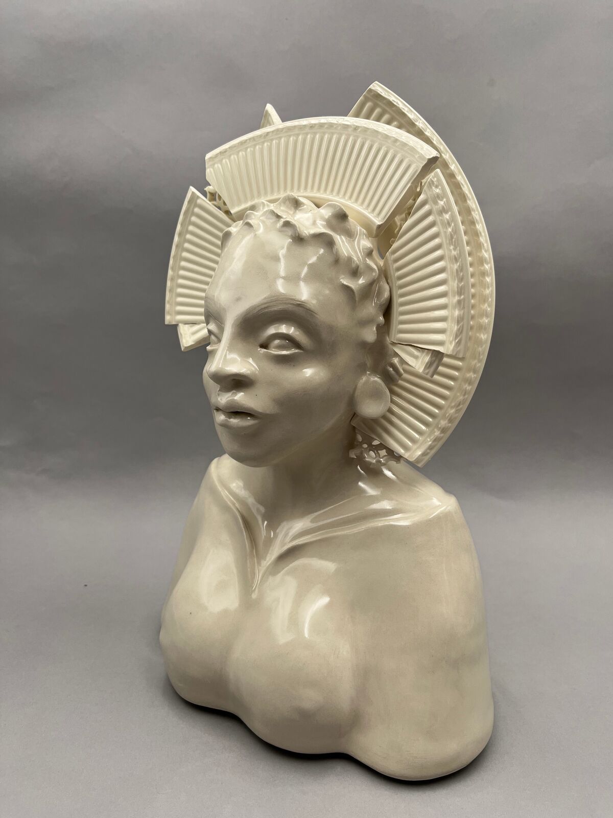 A glossy ceramic bust of a figure with an elaborate, segmented crown-like headpiece.