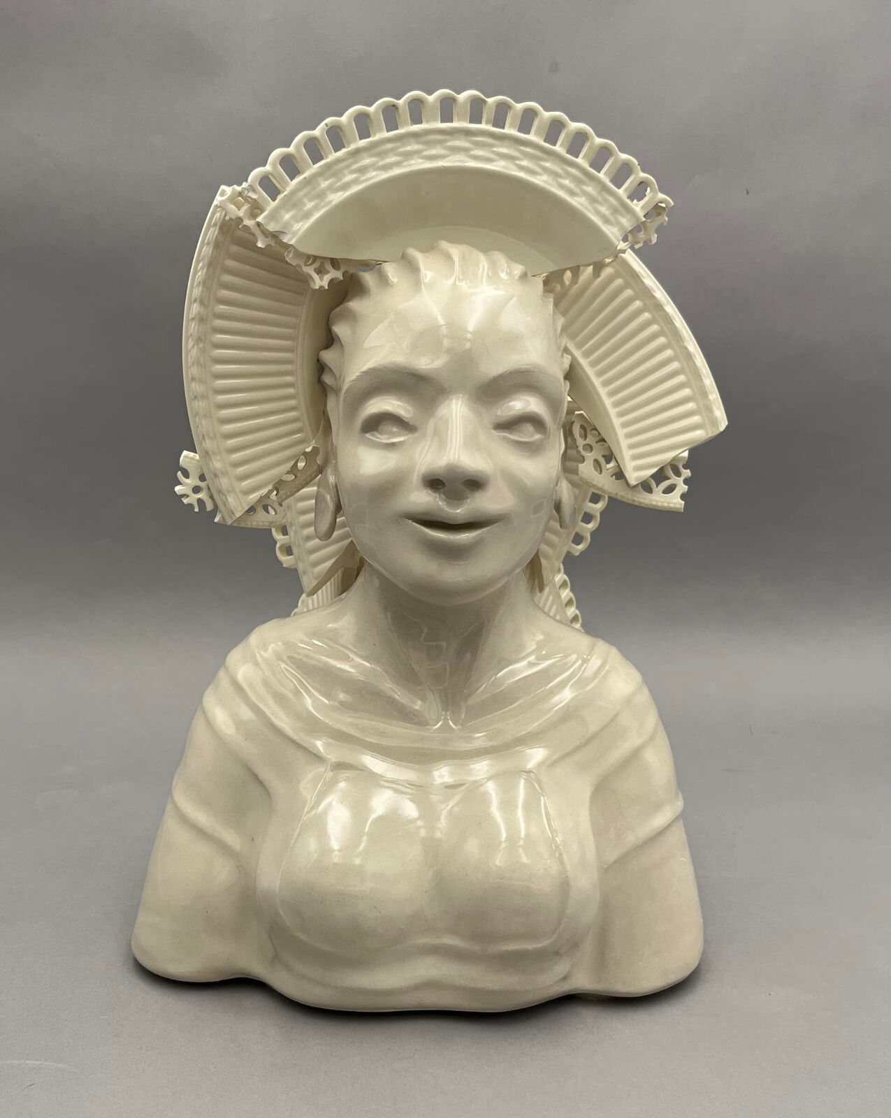 A glossy white ceramic bust of a figure wearing an elaborate, lacy headdress.