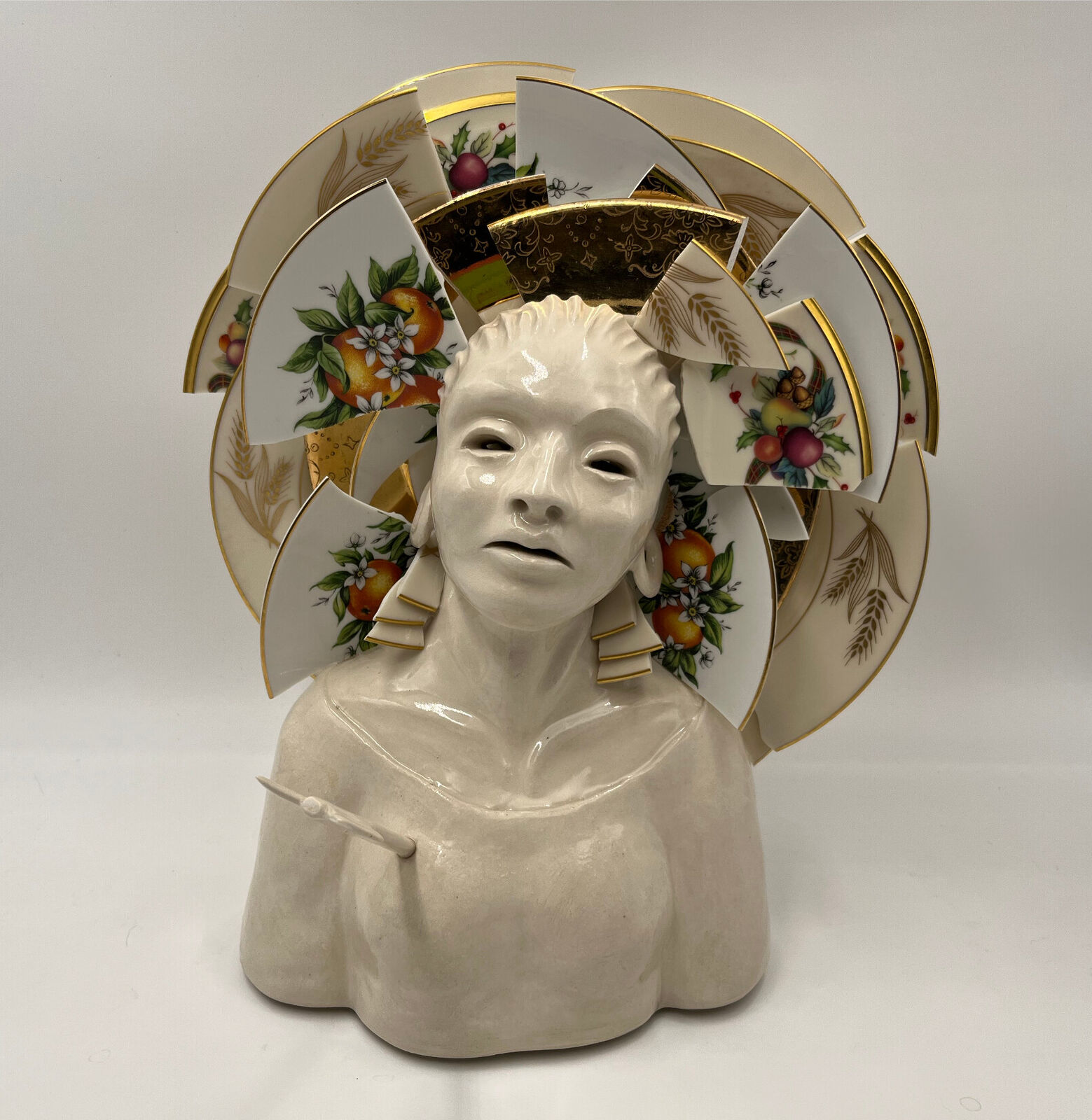 A ceramic bust adorned with a halo of broken, patterned porcelain plates.