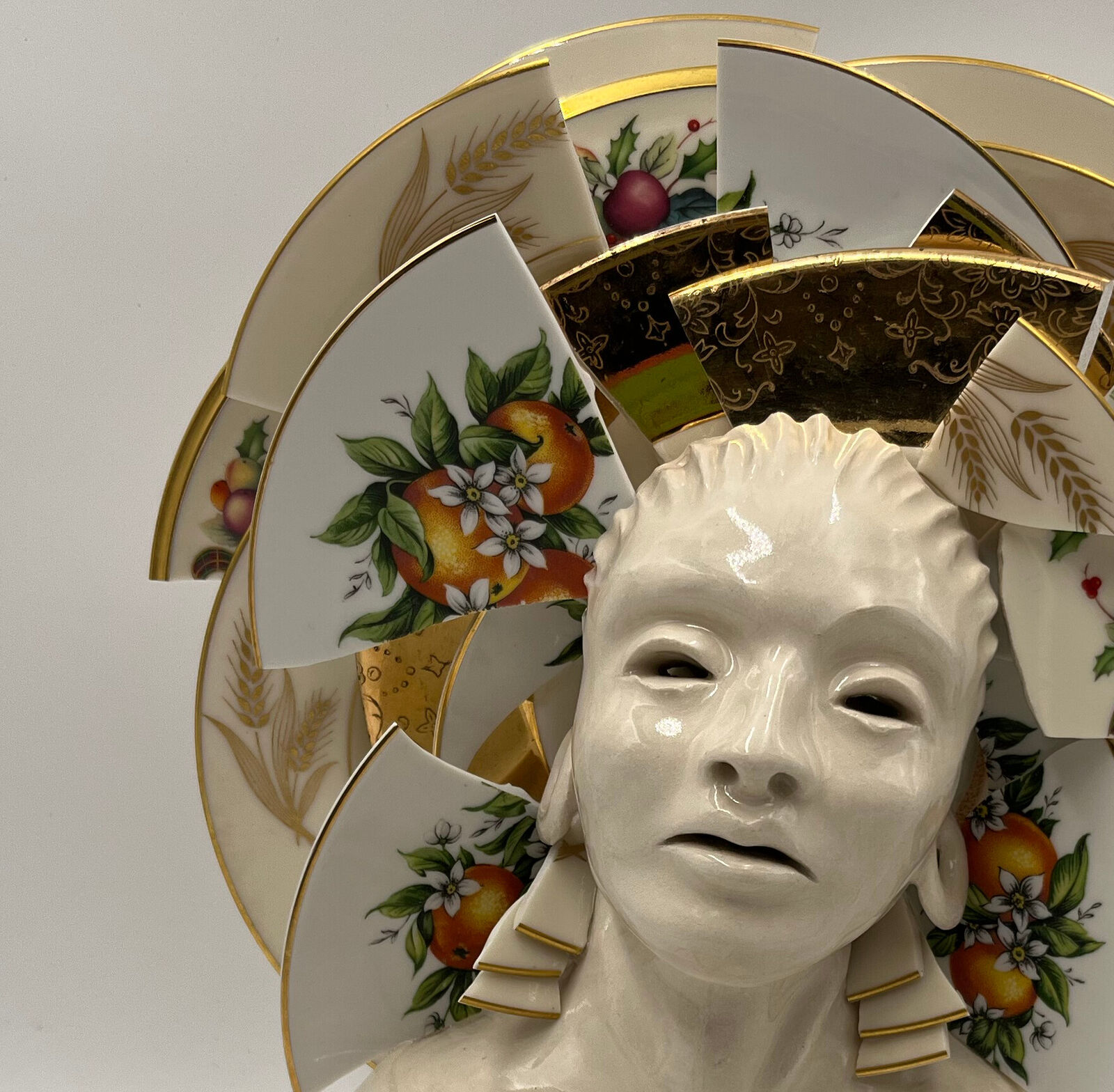 A ceramic bust adorned with a halo of broken, patterned porcelain plates.