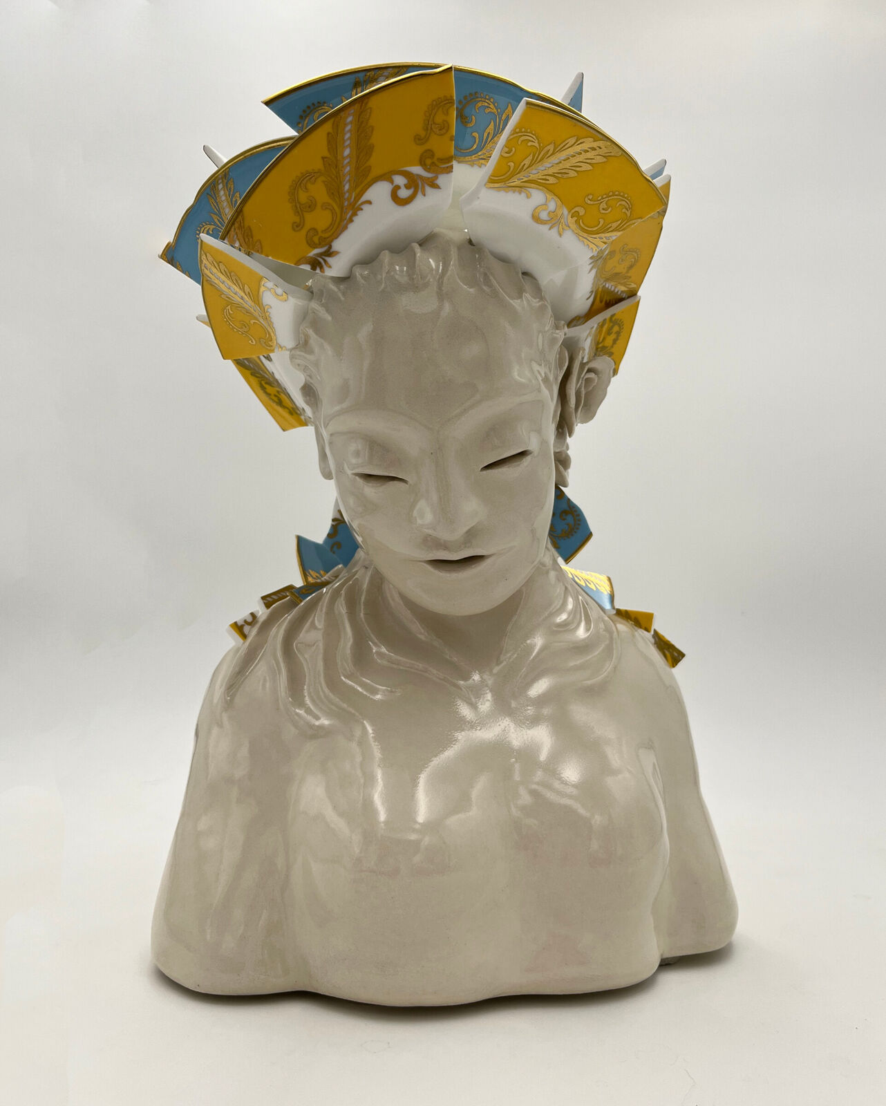 A glossy ceramic bust adorned with a crown of ornate, colorful plates.
