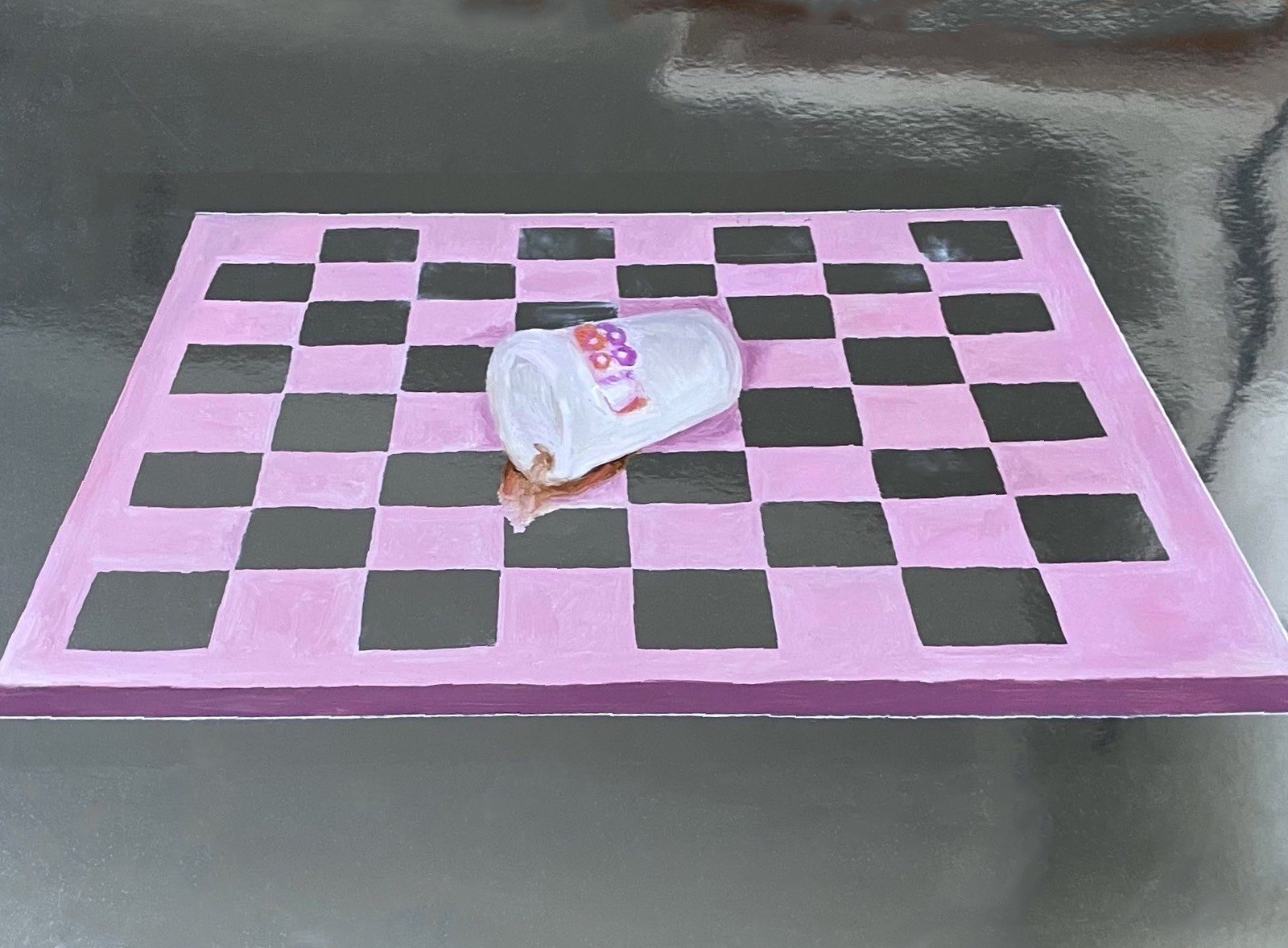 A white cup with colorful dots rests on a pink and black checkerboard surface.