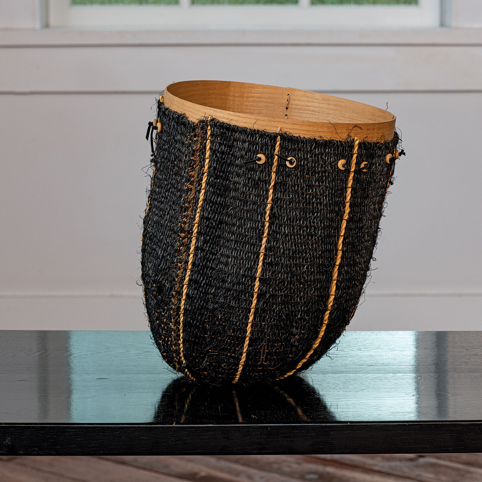 A woven basket with a wooden rim and natural rope accents sits on a dark reflective surface.
