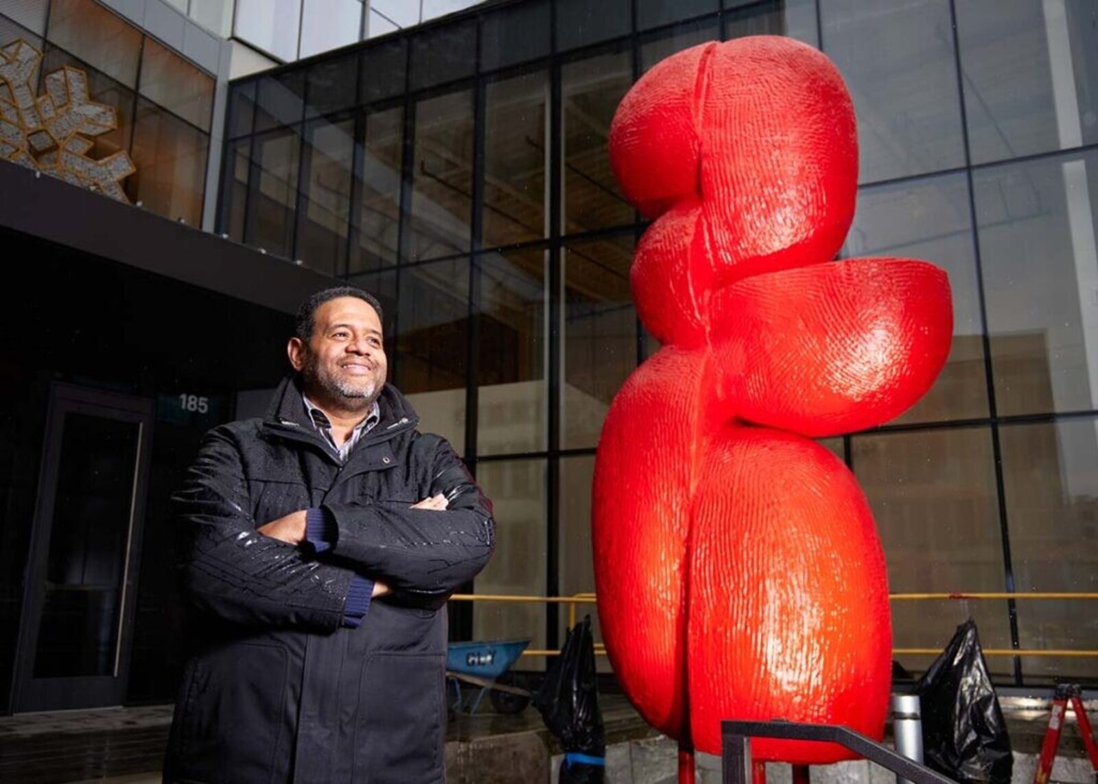 A bright red abstract sculpture stands in a lush garden.