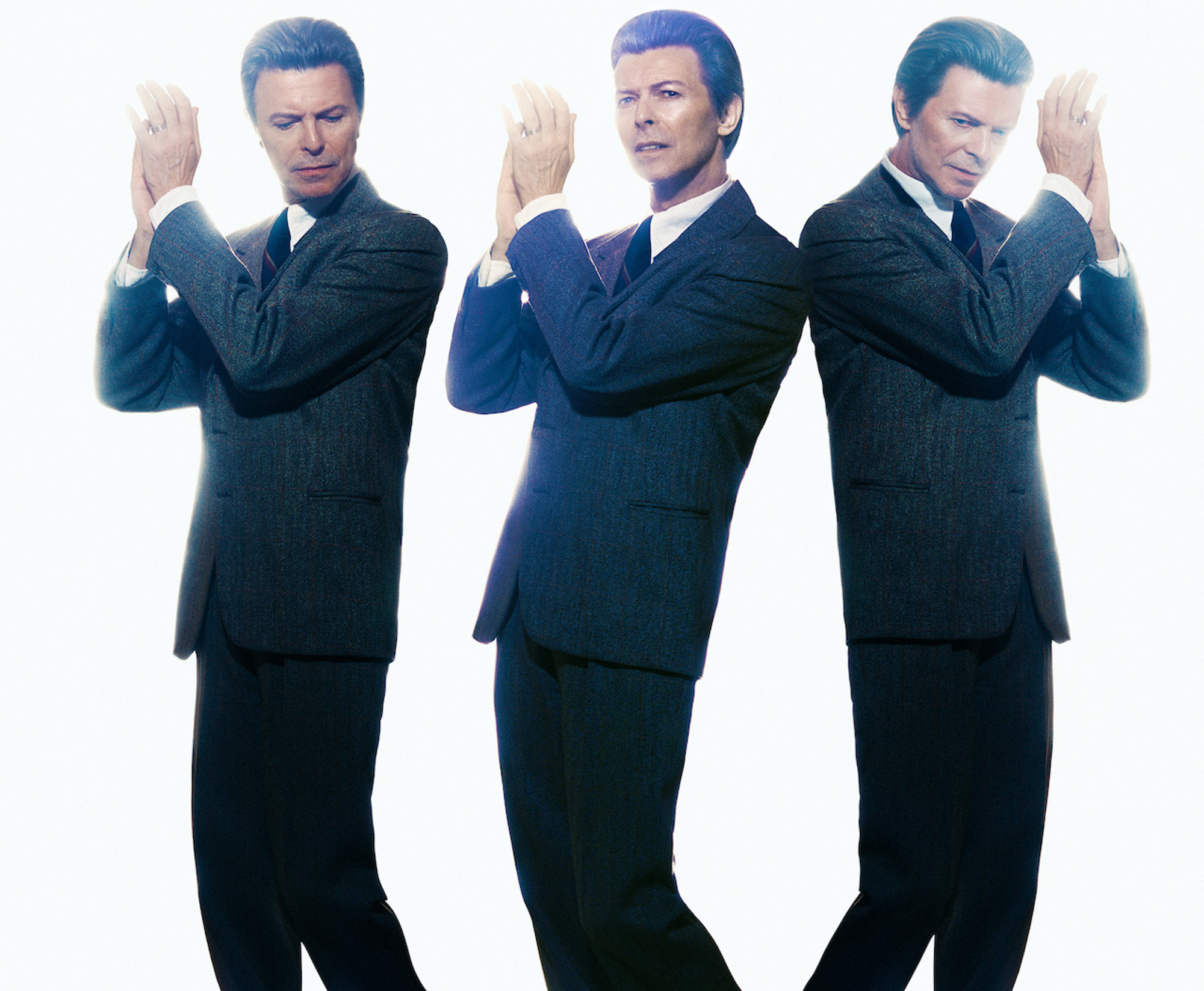 A group of three men in suits standing in a row with their hands in the air.