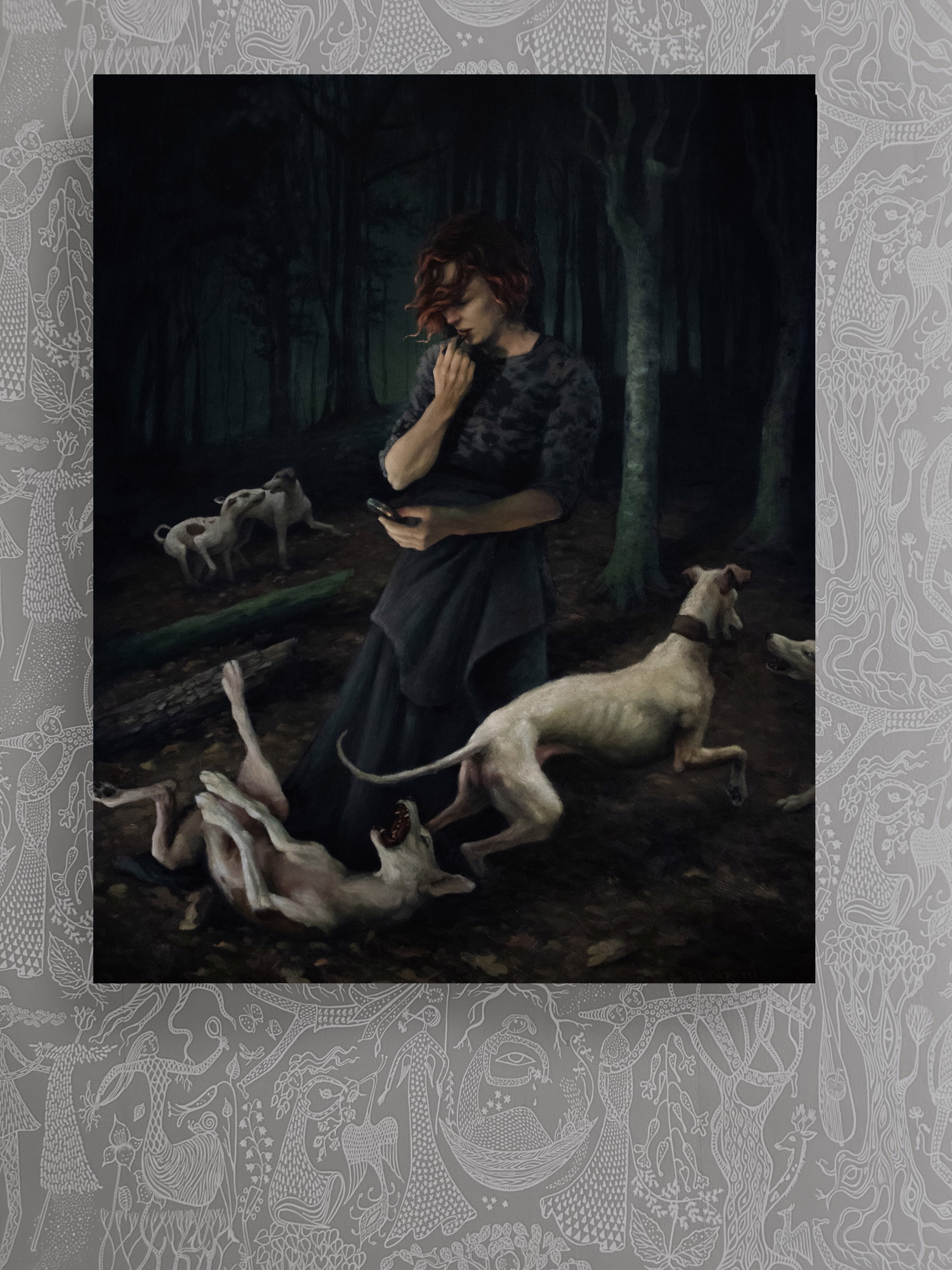 A woman standing in a forest with two dogs and a cell phone.