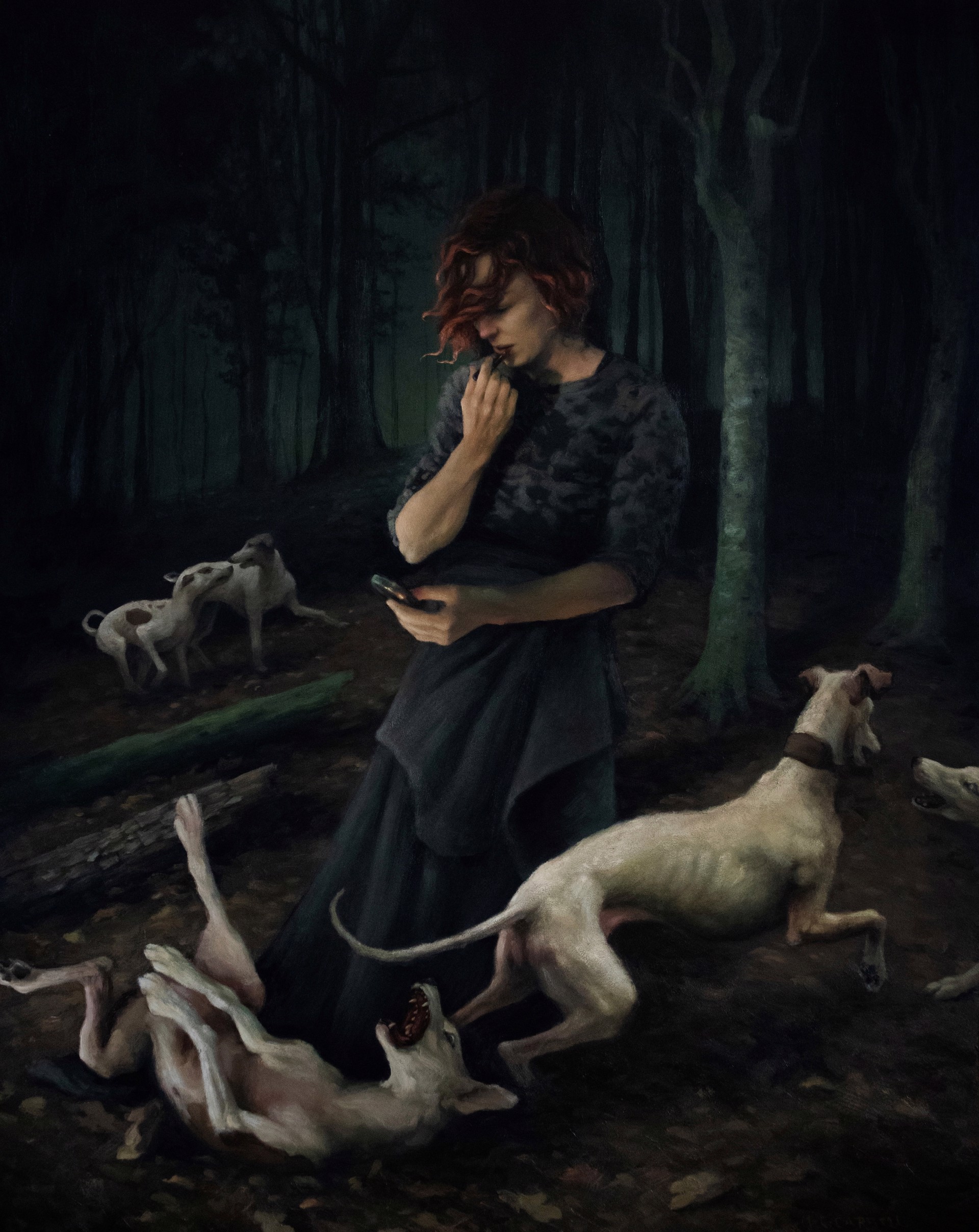 A woman standing in a forest with two dogs and a cell phone.
