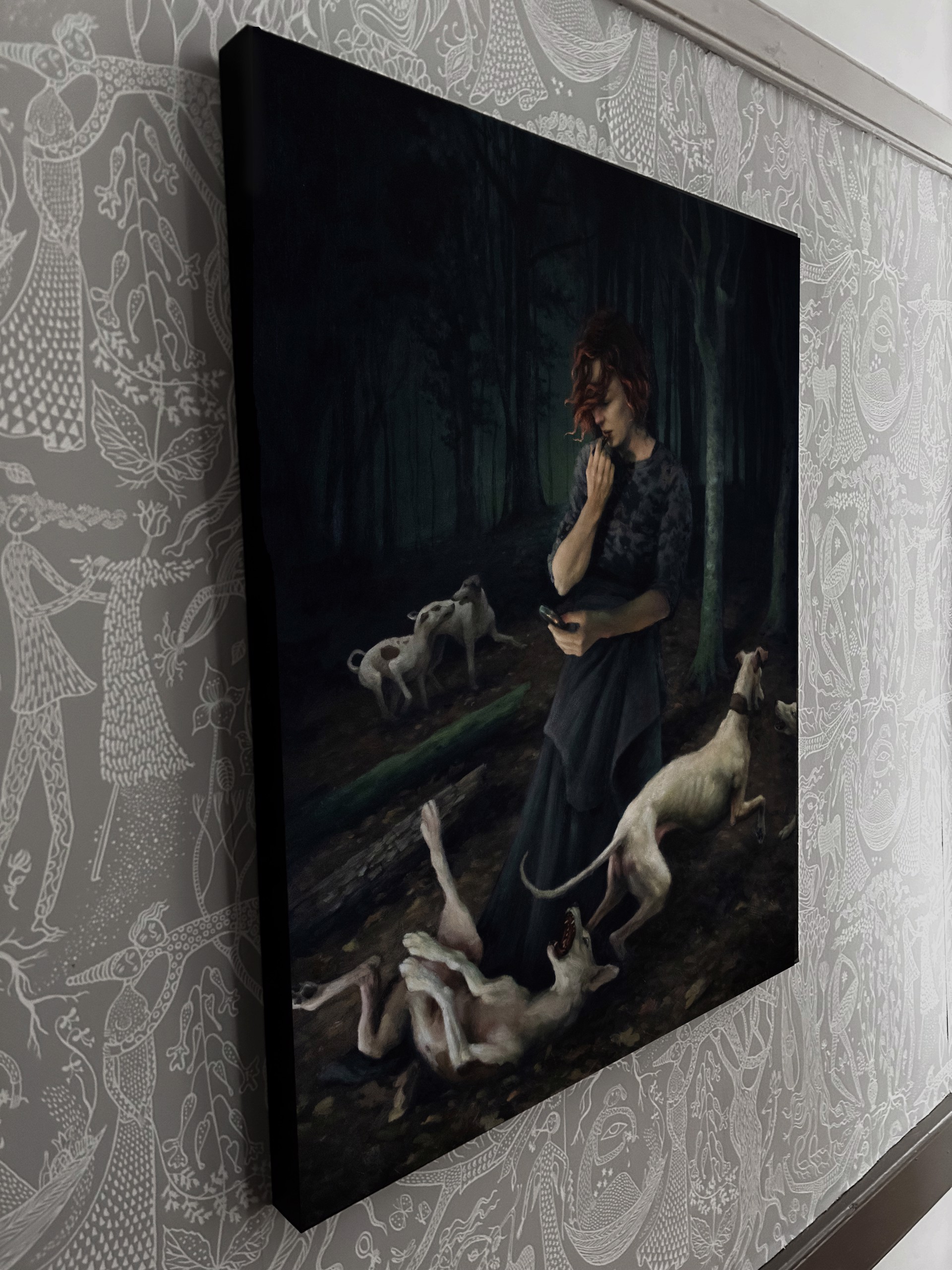 A woman standing in a forest with two dogs and a cell phone.