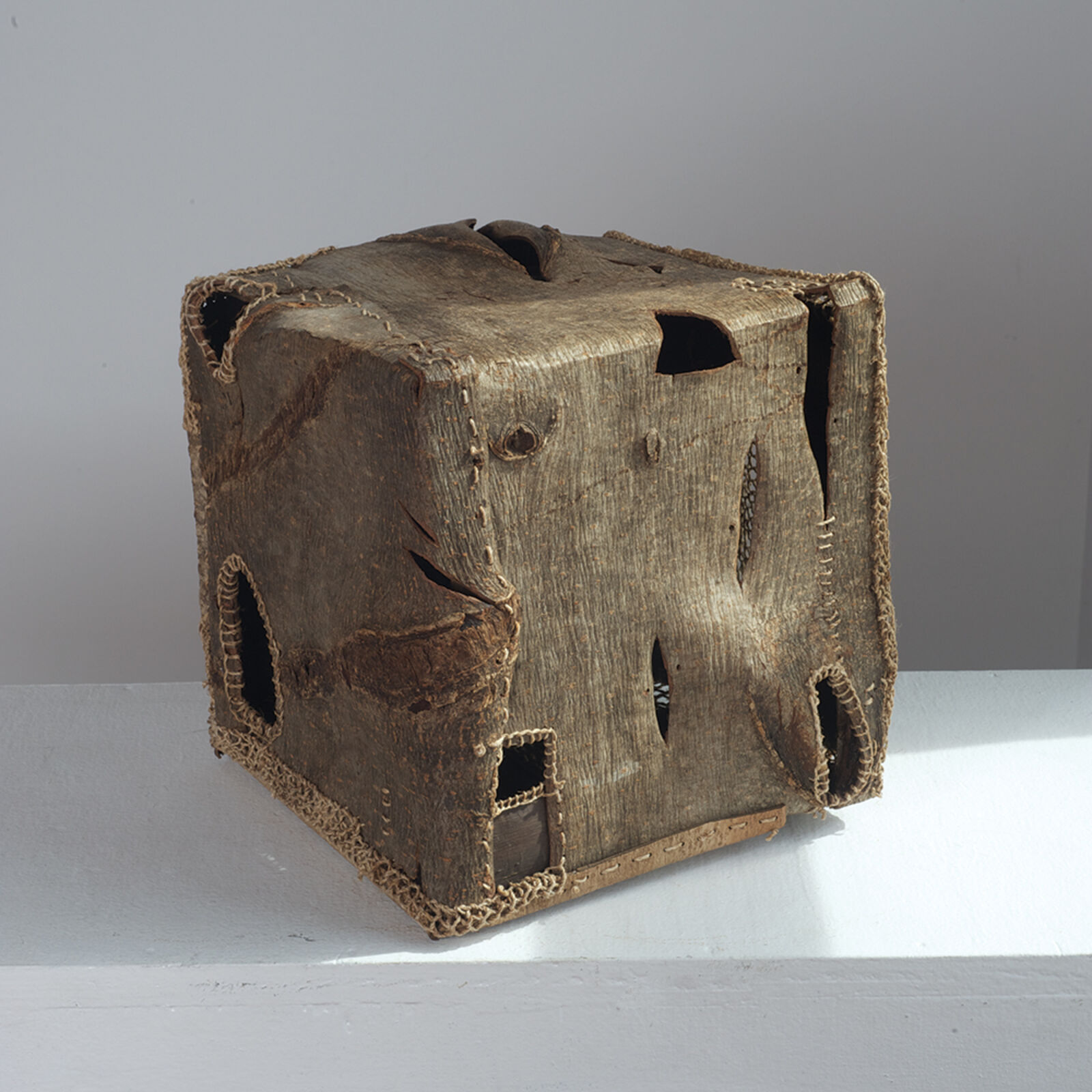 A weathered wooden cube with a rough, textured surface and visible holes.