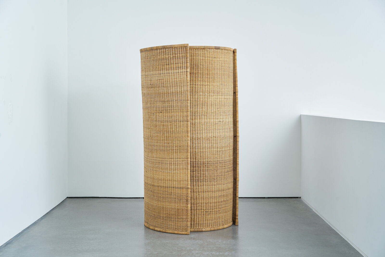 A room divider made out of woven rattan in a white room.