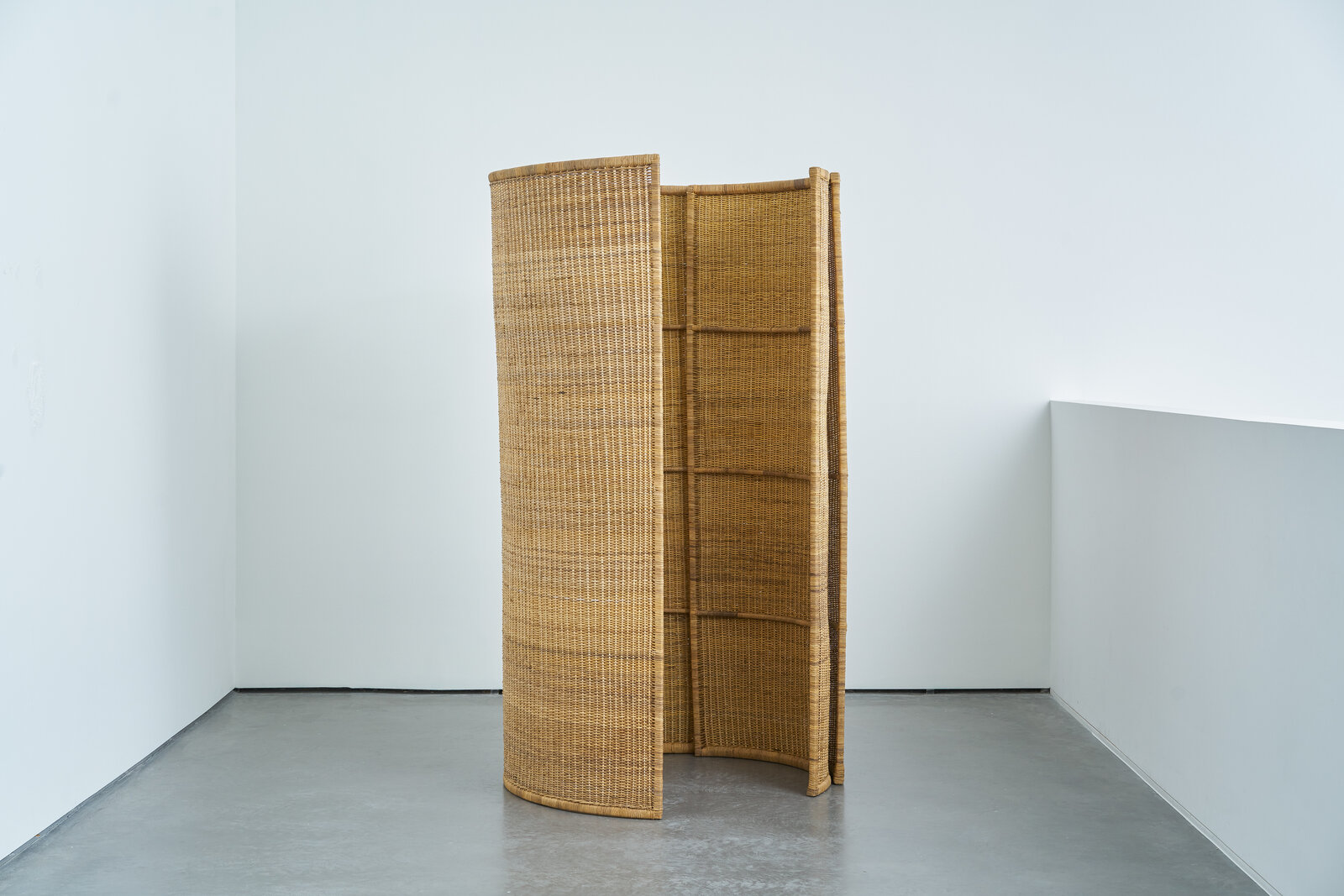 A room divider made out of woven rattan in a white room.