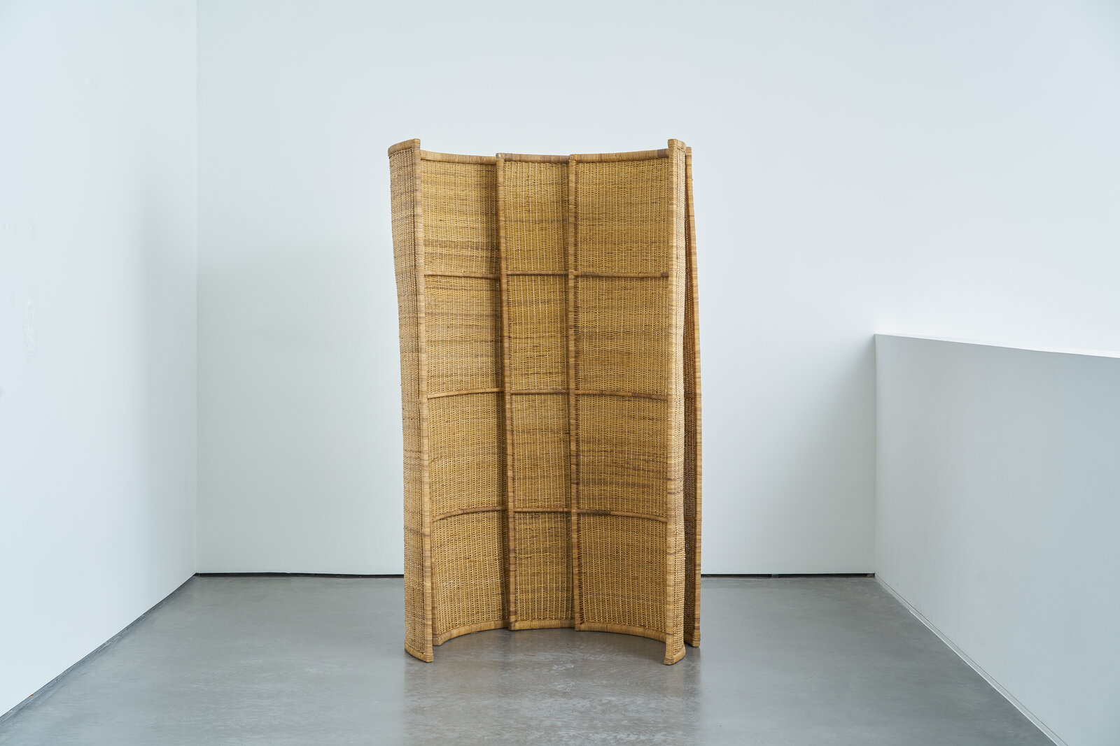 A room divider made out of woven rattan in a white room.