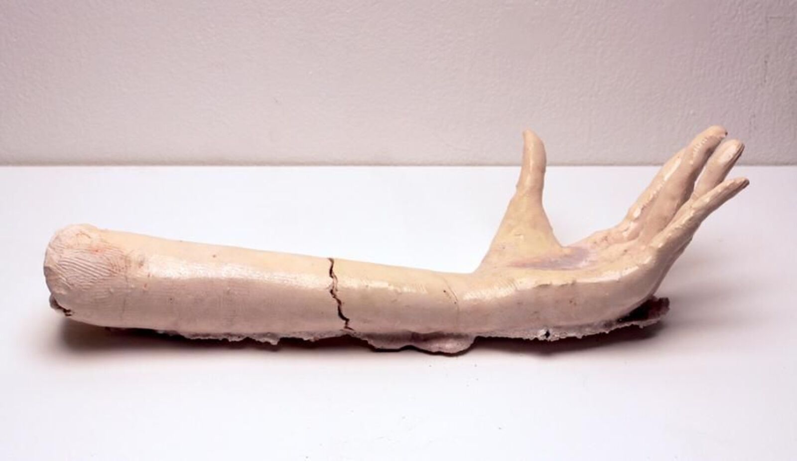 A pale, sculpted arm and hand resting on a white surface.