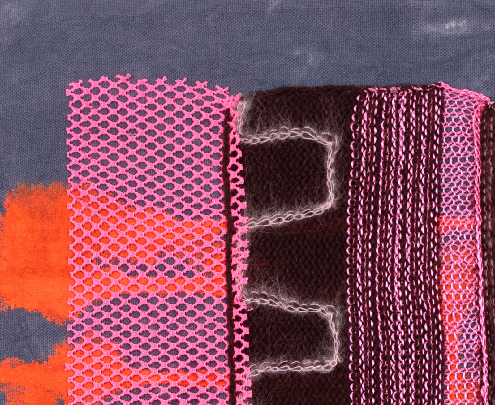 A mixed-media textile piece featuring a central brown knitted form with pink mesh, set against a grey background with orange and blue paint splatters.