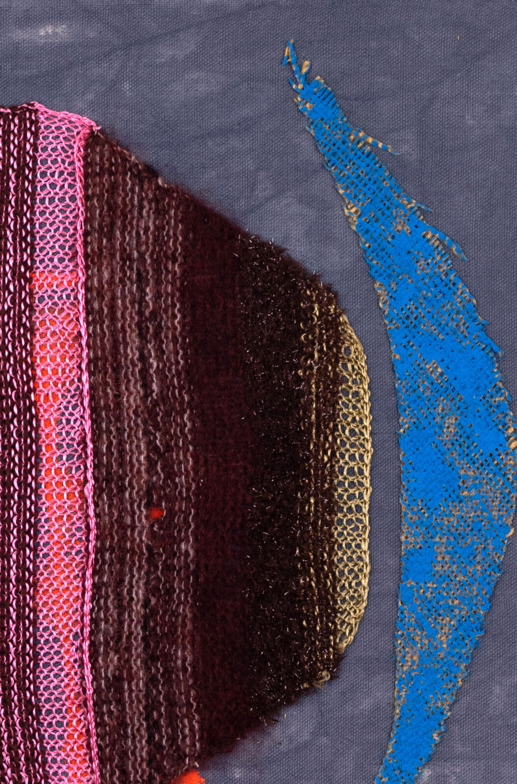 A mixed-media textile piece featuring a central brown knitted form with pink mesh, set against a grey background with orange and blue paint splatters.