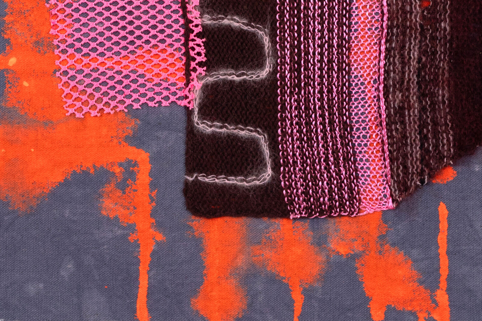 A mixed-media textile piece featuring a central brown knitted form with pink mesh, set against a grey background with orange and blue paint splatters.