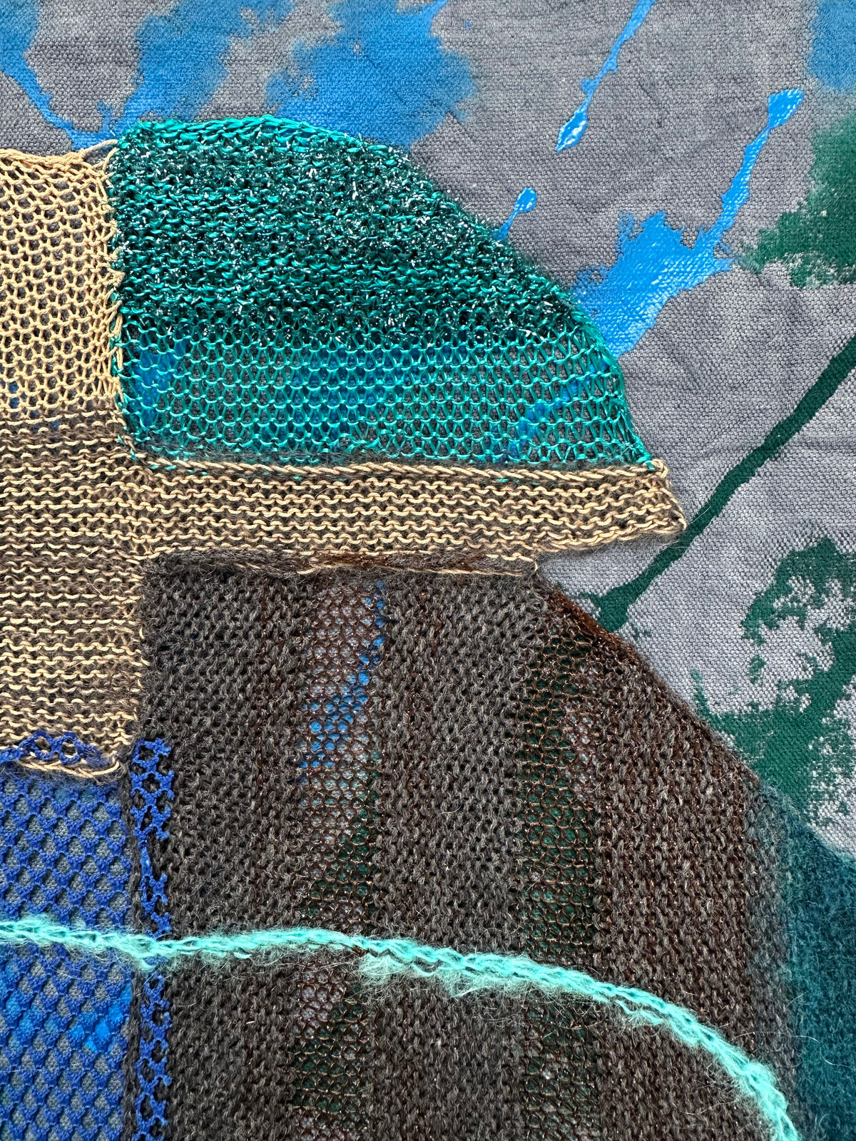 A textured textile artwork featuring a stylized helmet-like form against a tie-dye background.