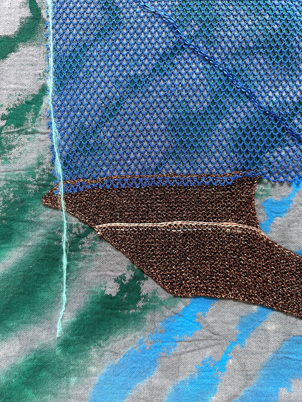 A textured textile artwork featuring a stylized helmet-like form against a tie-dye background.