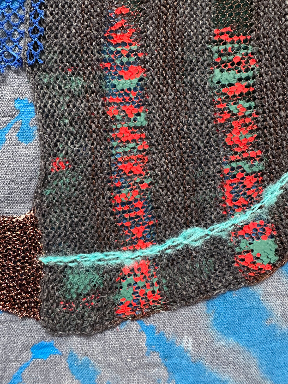 A textured textile artwork featuring a stylized helmet-like form against a tie-dye background.