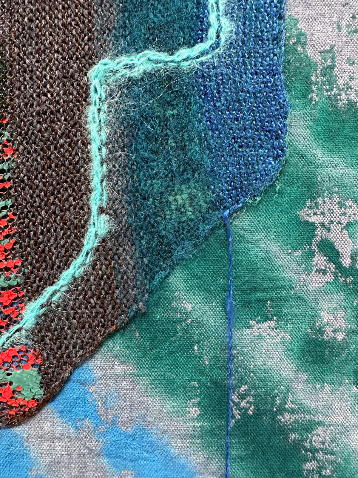 A textured textile artwork featuring a stylized helmet-like form against a tie-dye background.
