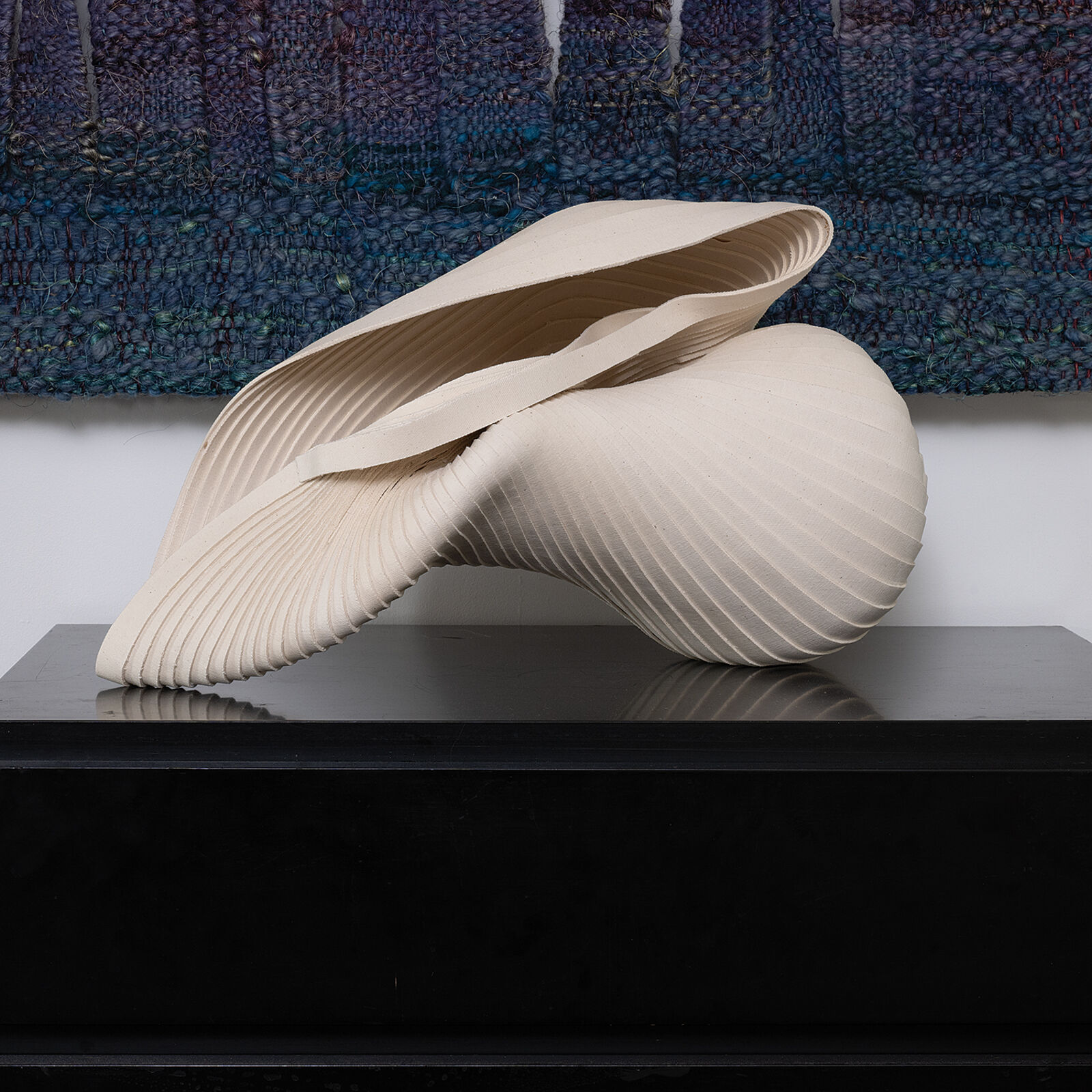 A sculptural piece resembling a folded shell or abstract flower resting on a reflective dark surface.