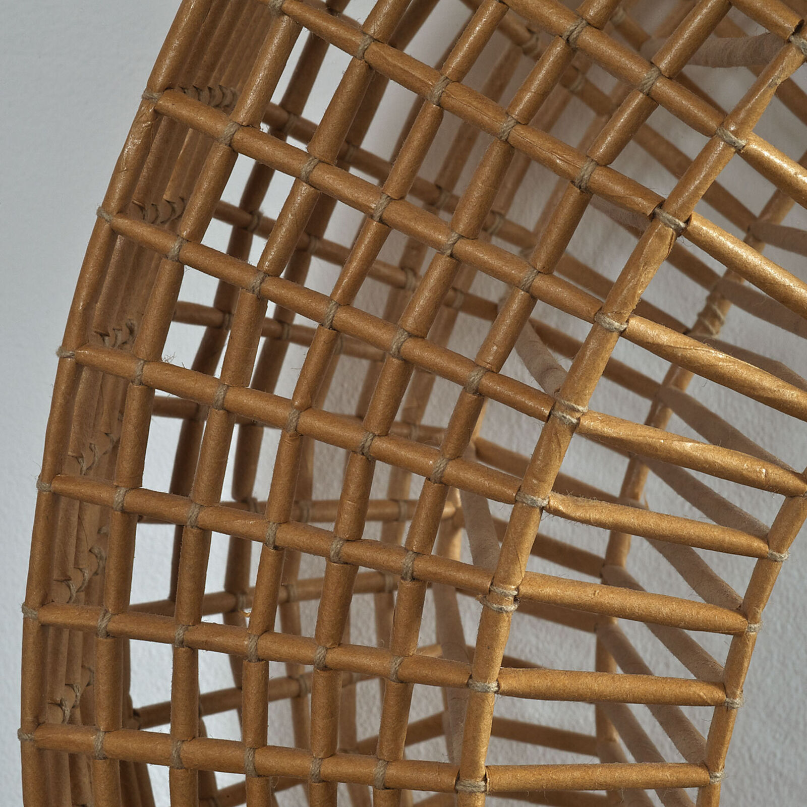 A woven spiral sculpture in warm earth tones against a plain white wall.