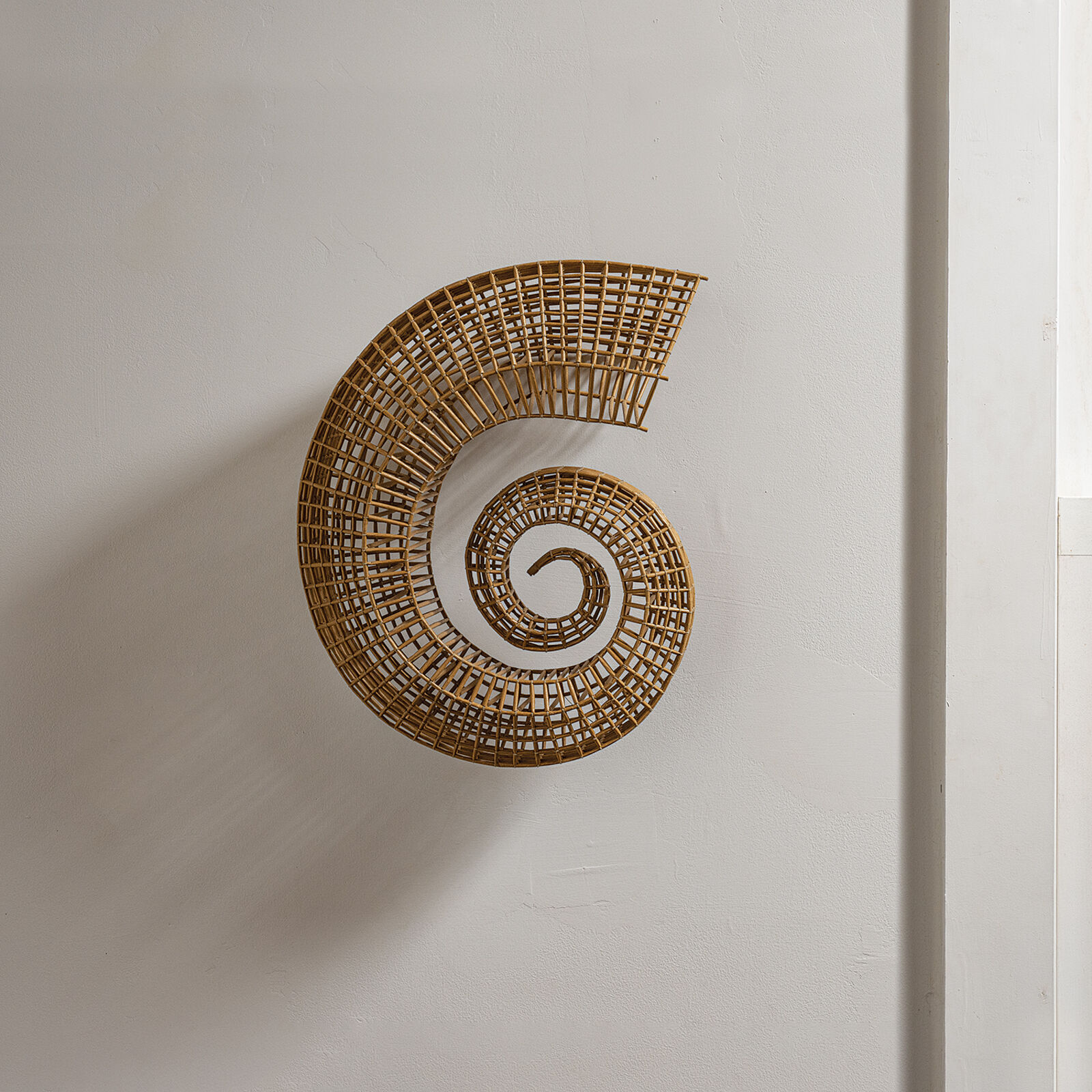 A woven spiral sculpture in warm earth tones against a plain white wall.