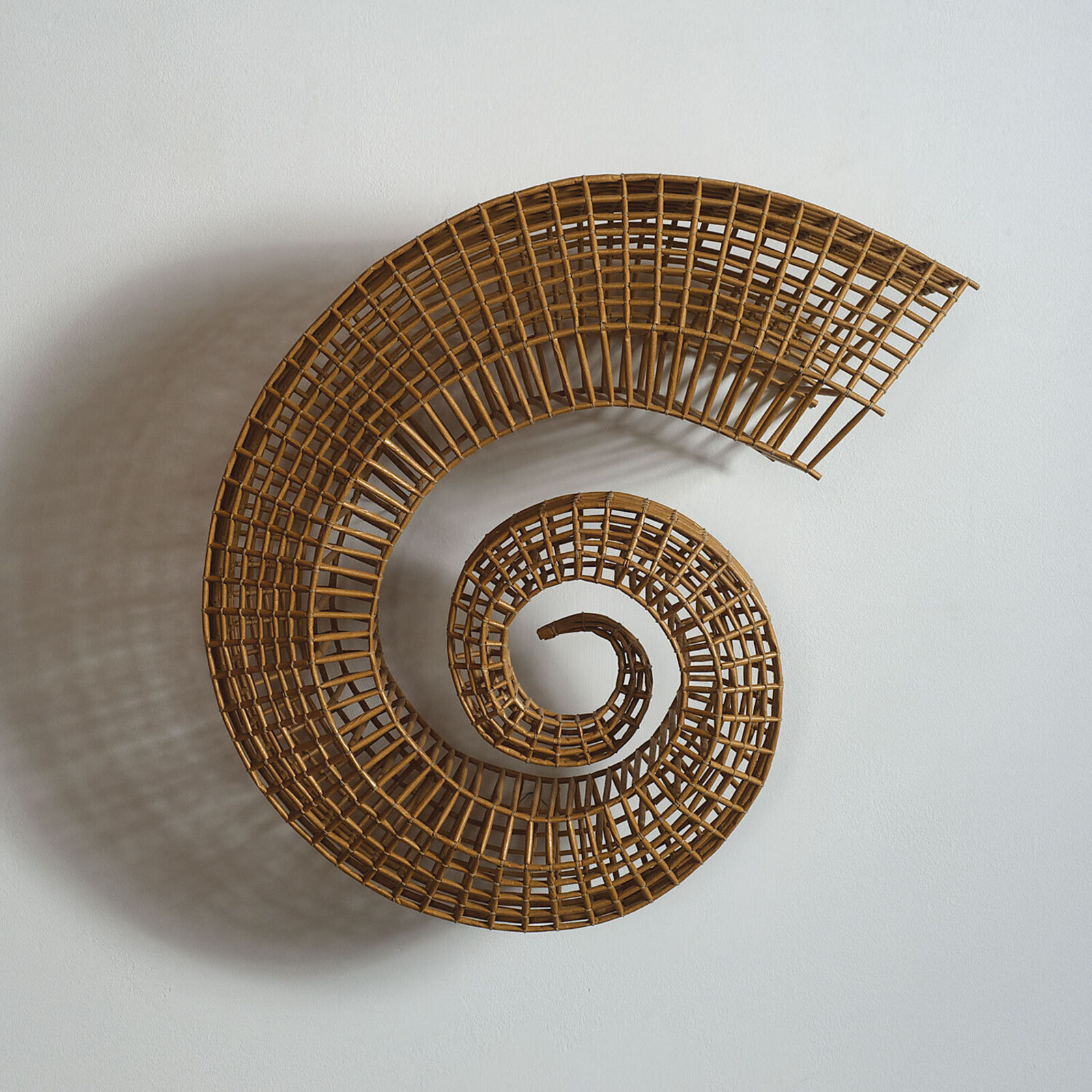 A woven spiral sculpture in warm earth tones against a plain white wall.