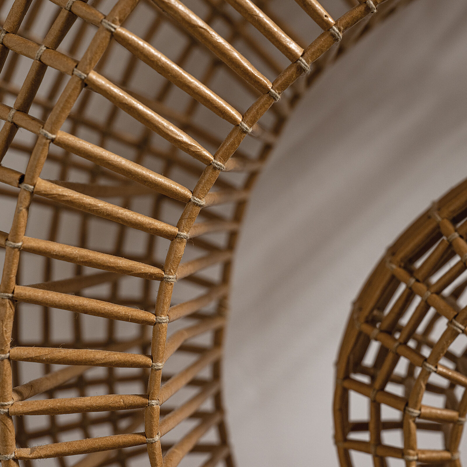 A woven spiral sculpture in warm earth tones against a plain white wall.