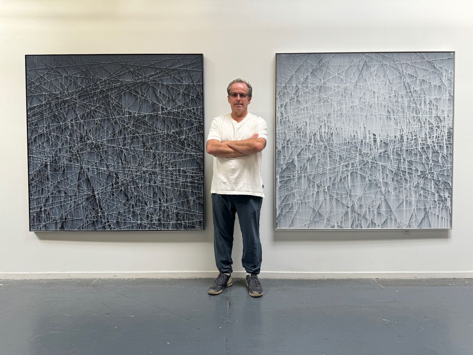 A textured abstract artwork featuring a dark, charcoal surface crisscrossed with fine white lines.