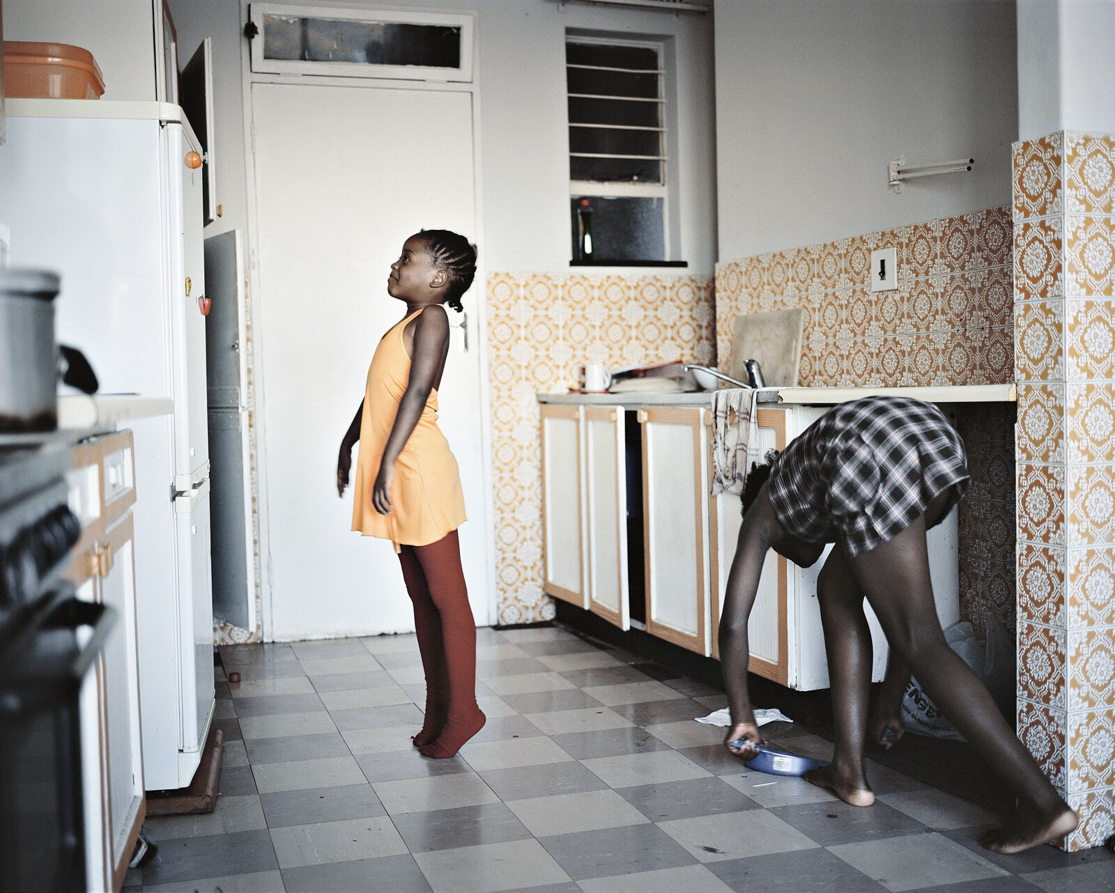 Two women in a kitchen with a woman bending over to pick up something.
