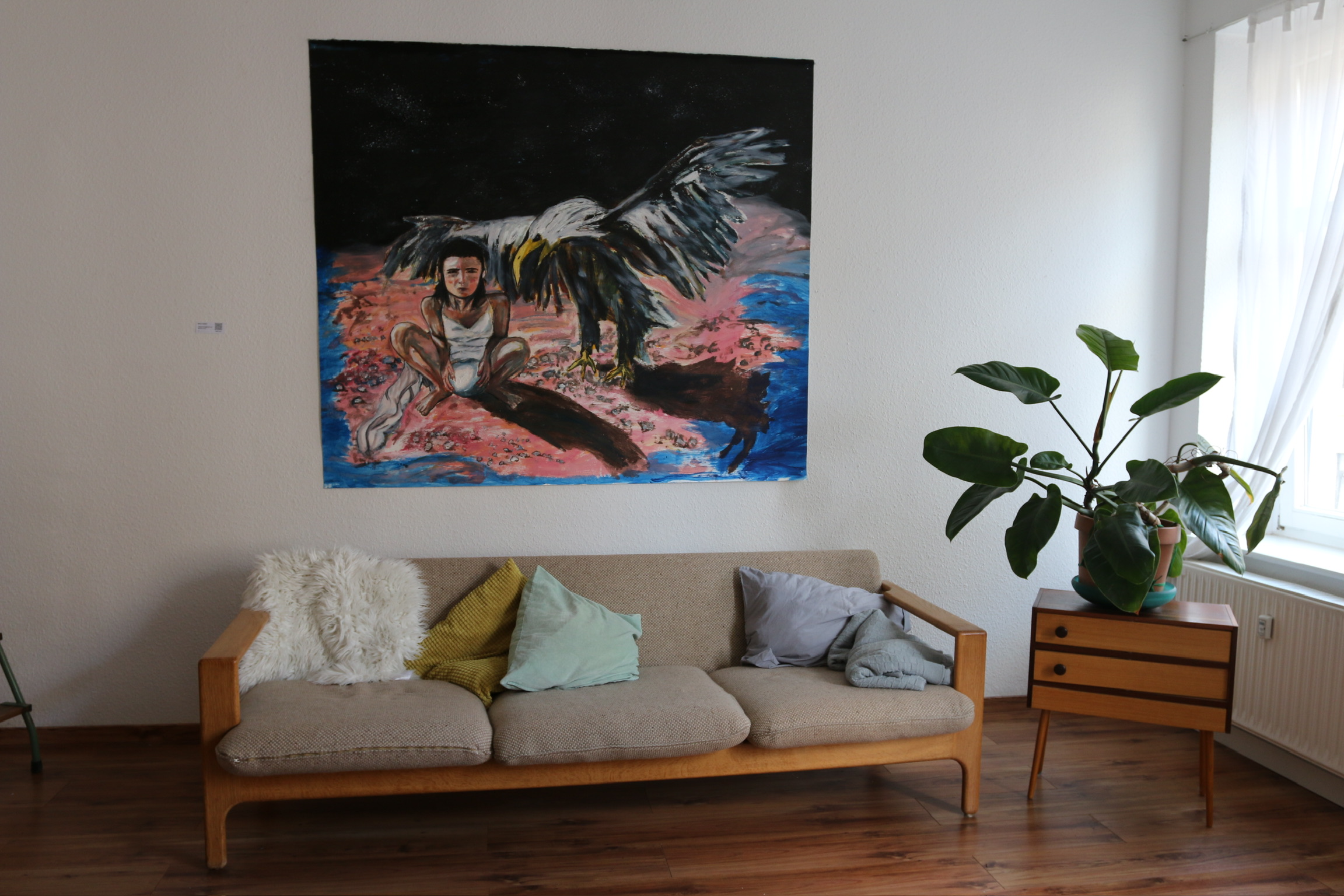 A somber figure sits beside a large bird with outstretched wings against a dark, textured background.