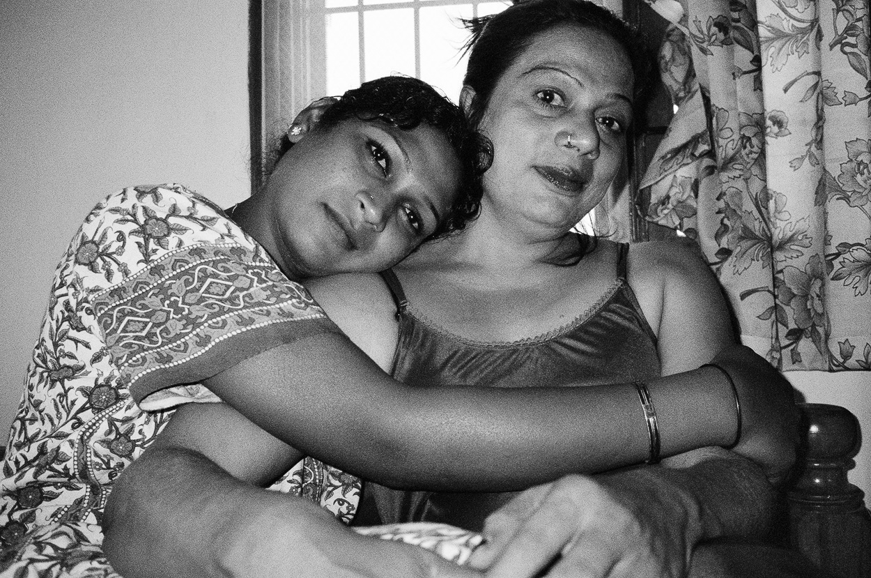 A woman and a young girl hugging each other on a bed.