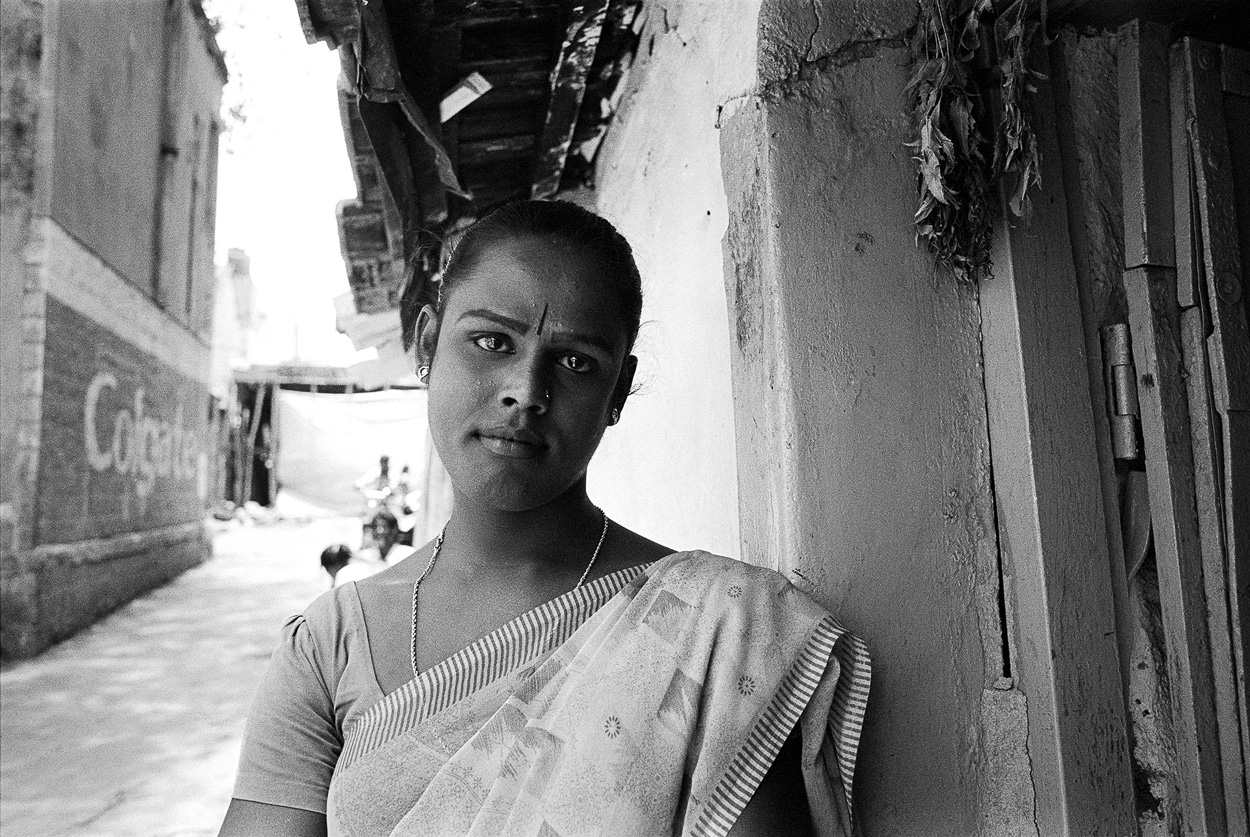 A woman in a white sari leaning against a wall.