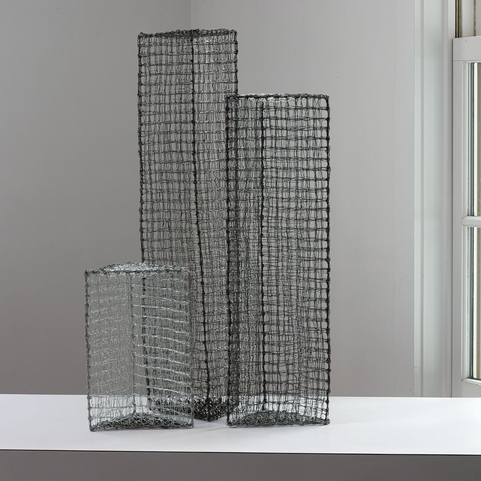A minimalist composition of three wire mesh vases in varying heights.