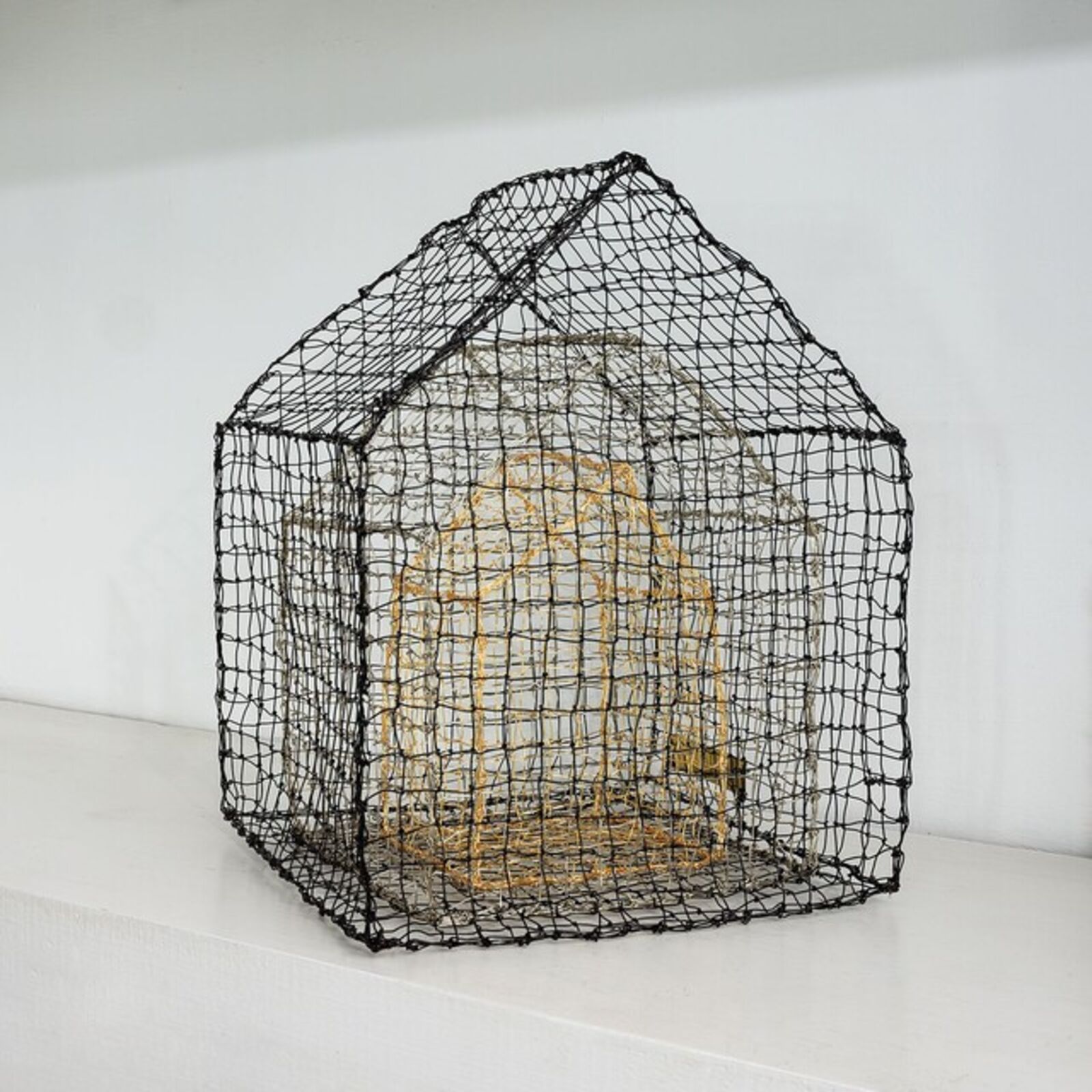 A wireframe house sculpture with a golden interior structure.